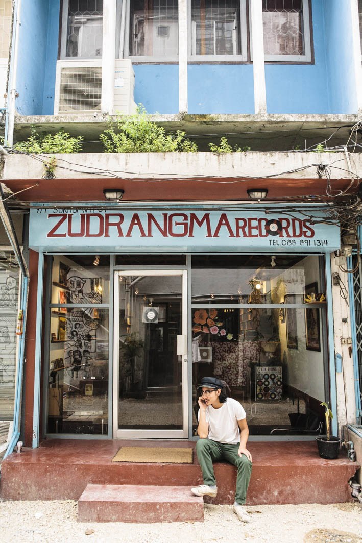 Person sitting outside ZudRangMa Records storefront in Bangkok with blue signage and vinyl records visible inside
