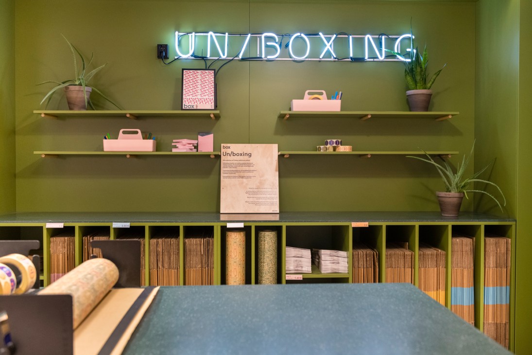 Box by Posti storefront interior in Helsinki with neon 'UNBOXING' sign, wooden shelving, potted plants, and pink organizational boxes.