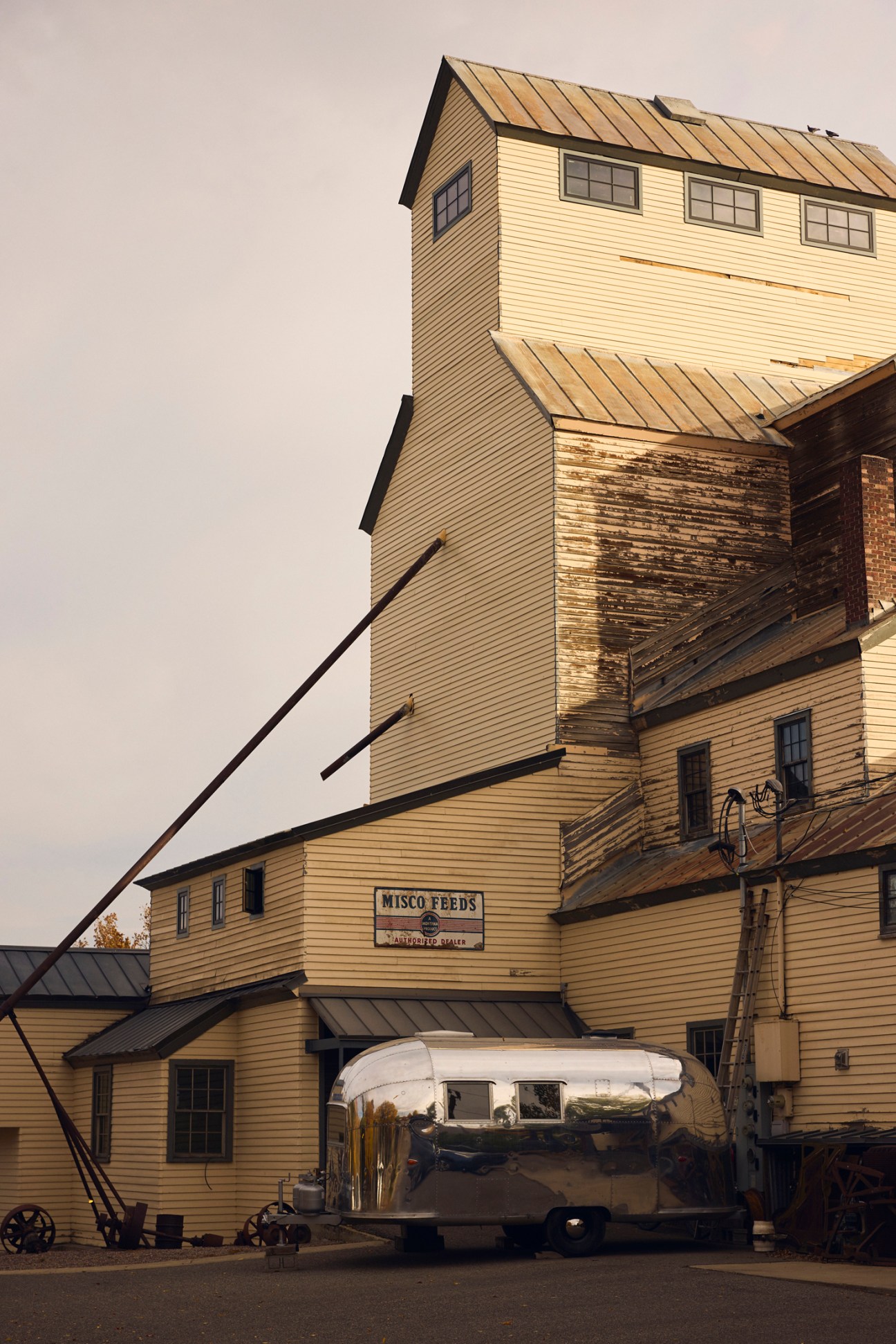 Historic wooden grain elevator with Misco Feeds signage and vintage Airstream trailer parked below