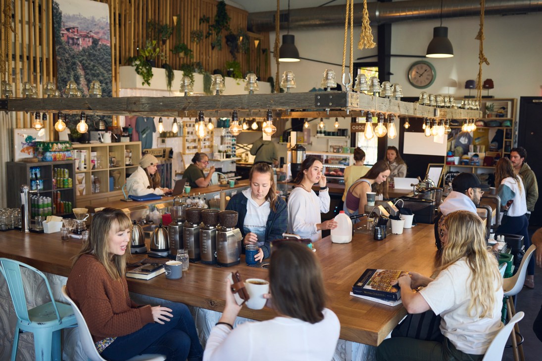 Interior of a modern coffee shop with customers seated at a wooden counter and tables.