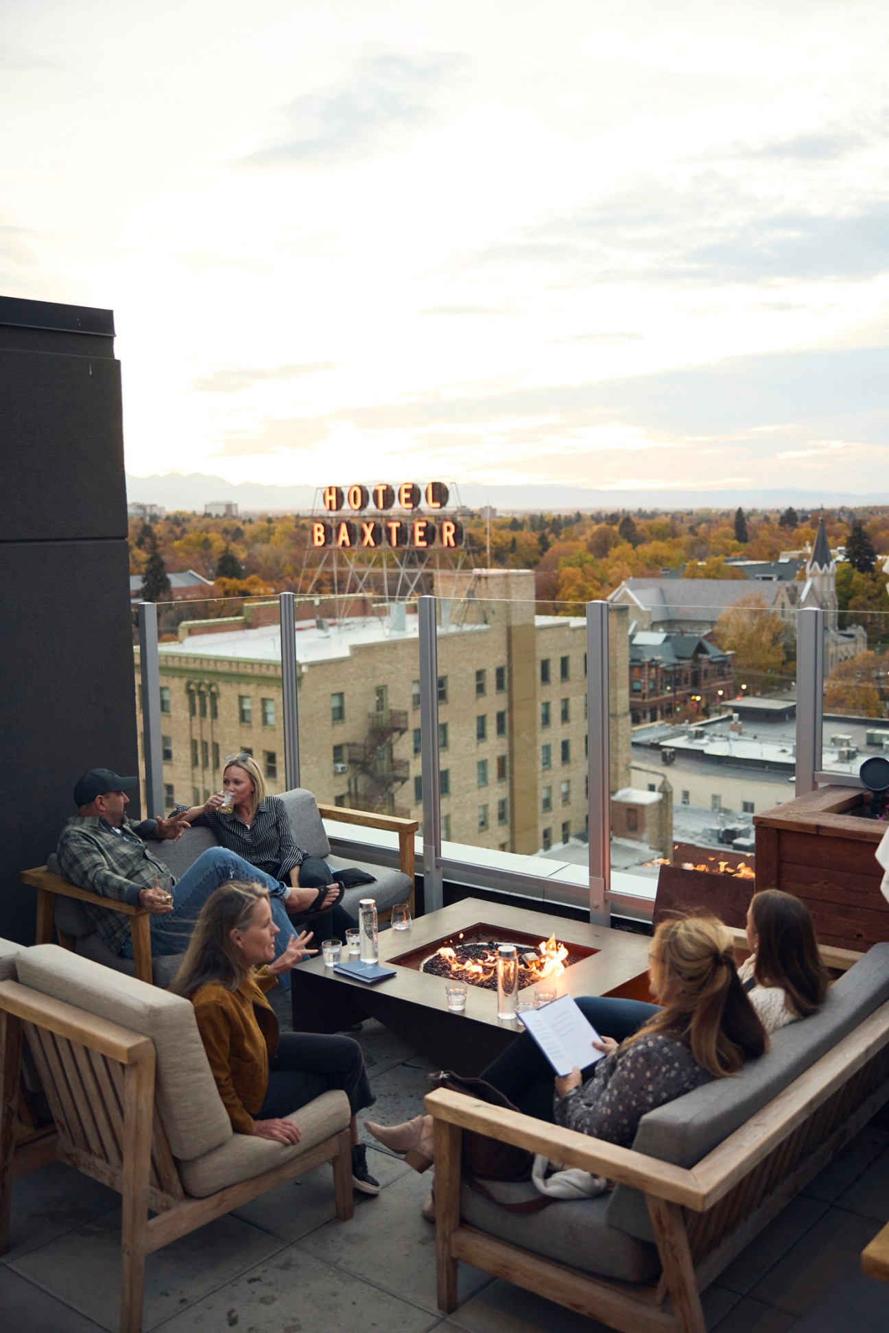 People relaxing on a rooftop terrace with Hotel Baxter sign visible in the background cityscape.