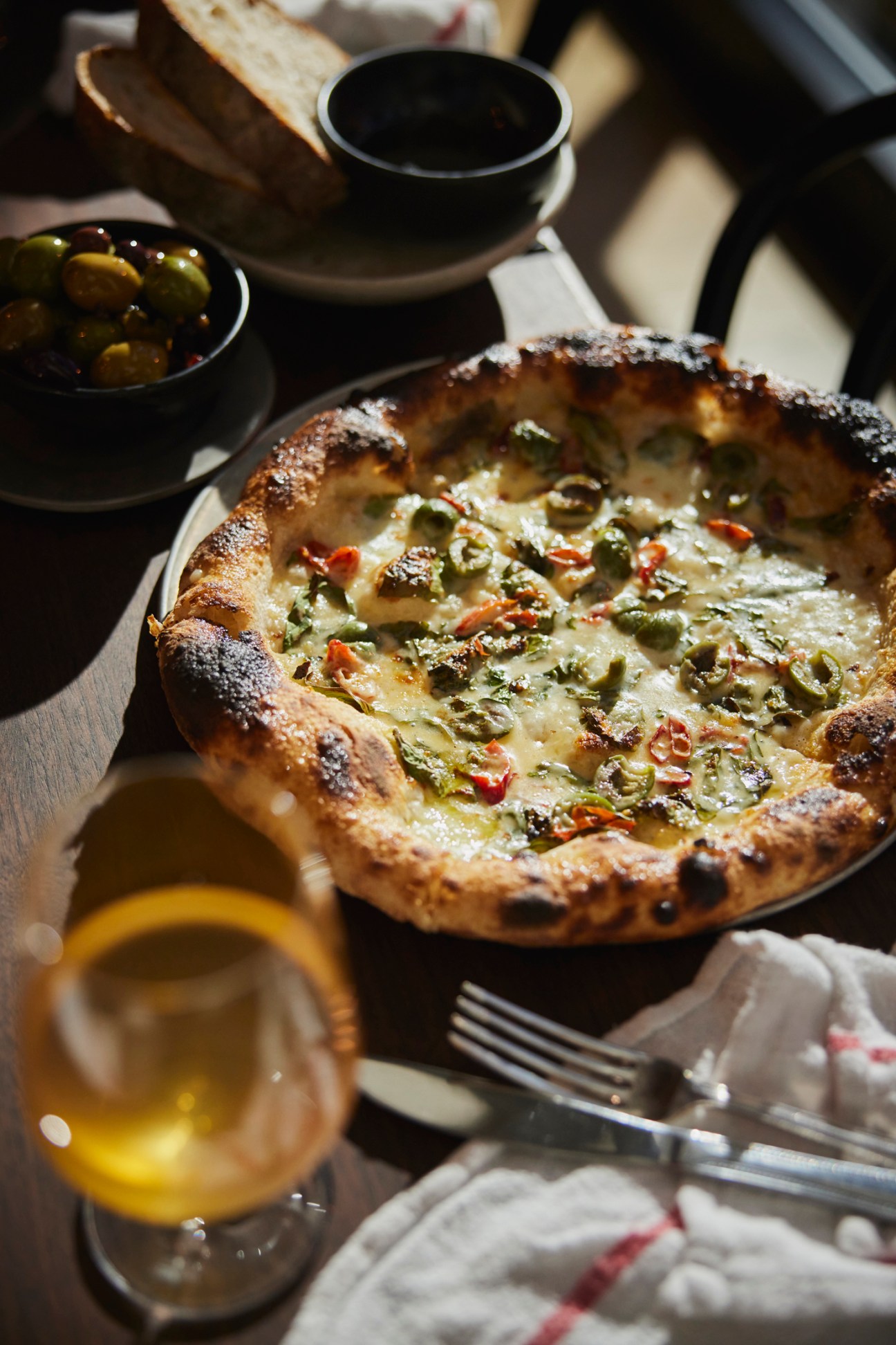 Sourdough bread topped with capers and herbs on a dining table with olives and wine.