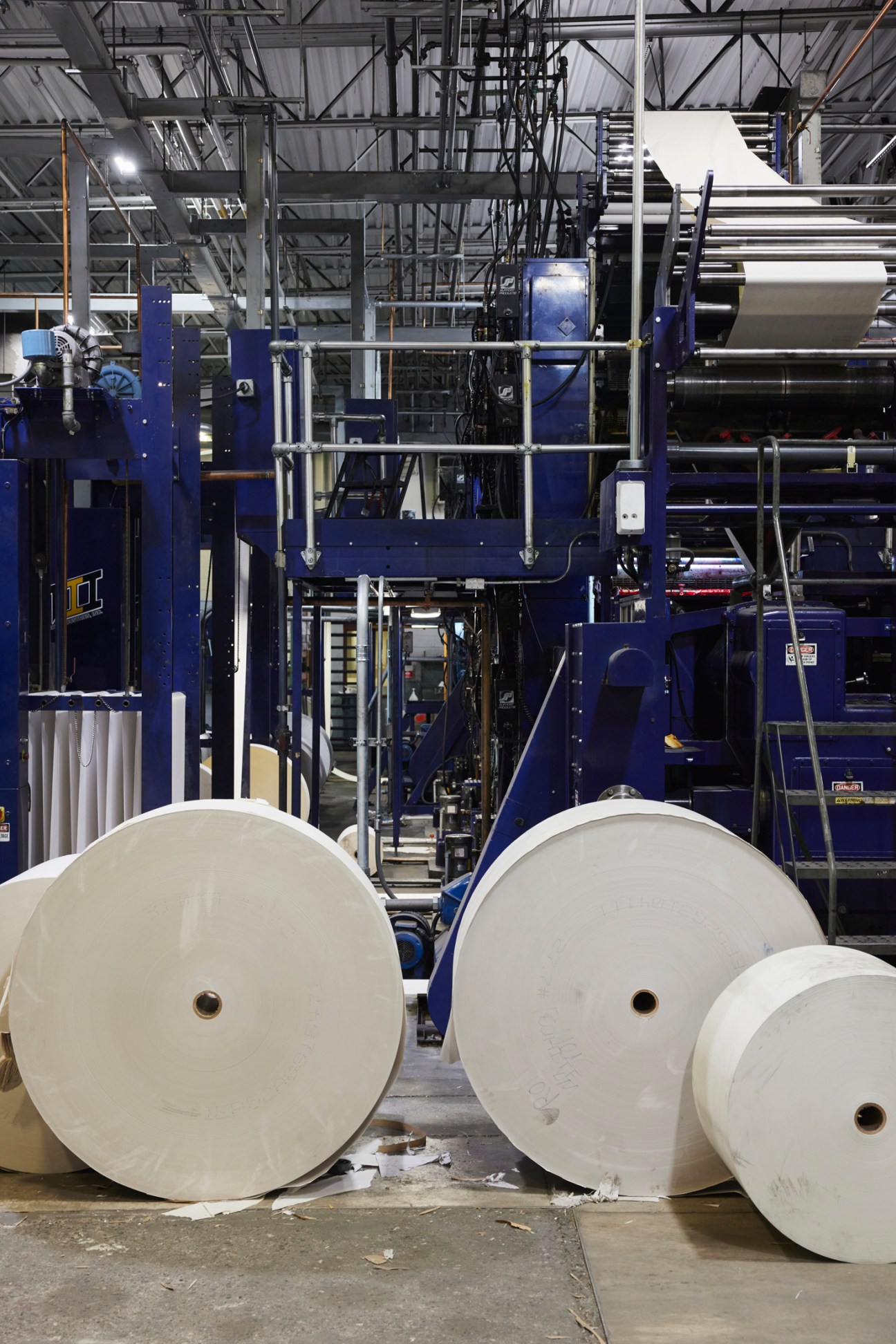 Industrial manufacturing facility with large white paper or textile rolls in foreground and blue machinery in background.