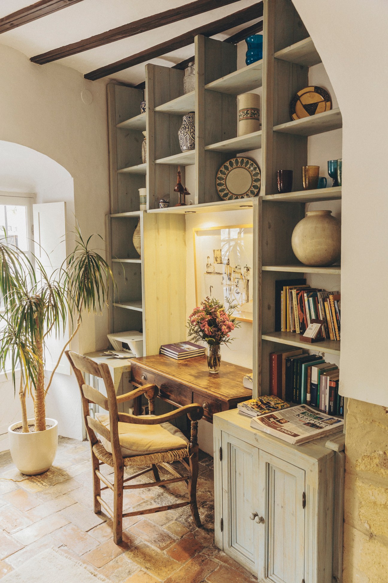 A cozy study nook with built-in bookshelves, wooden desk, woven chair, and warm lighting in rustic interior