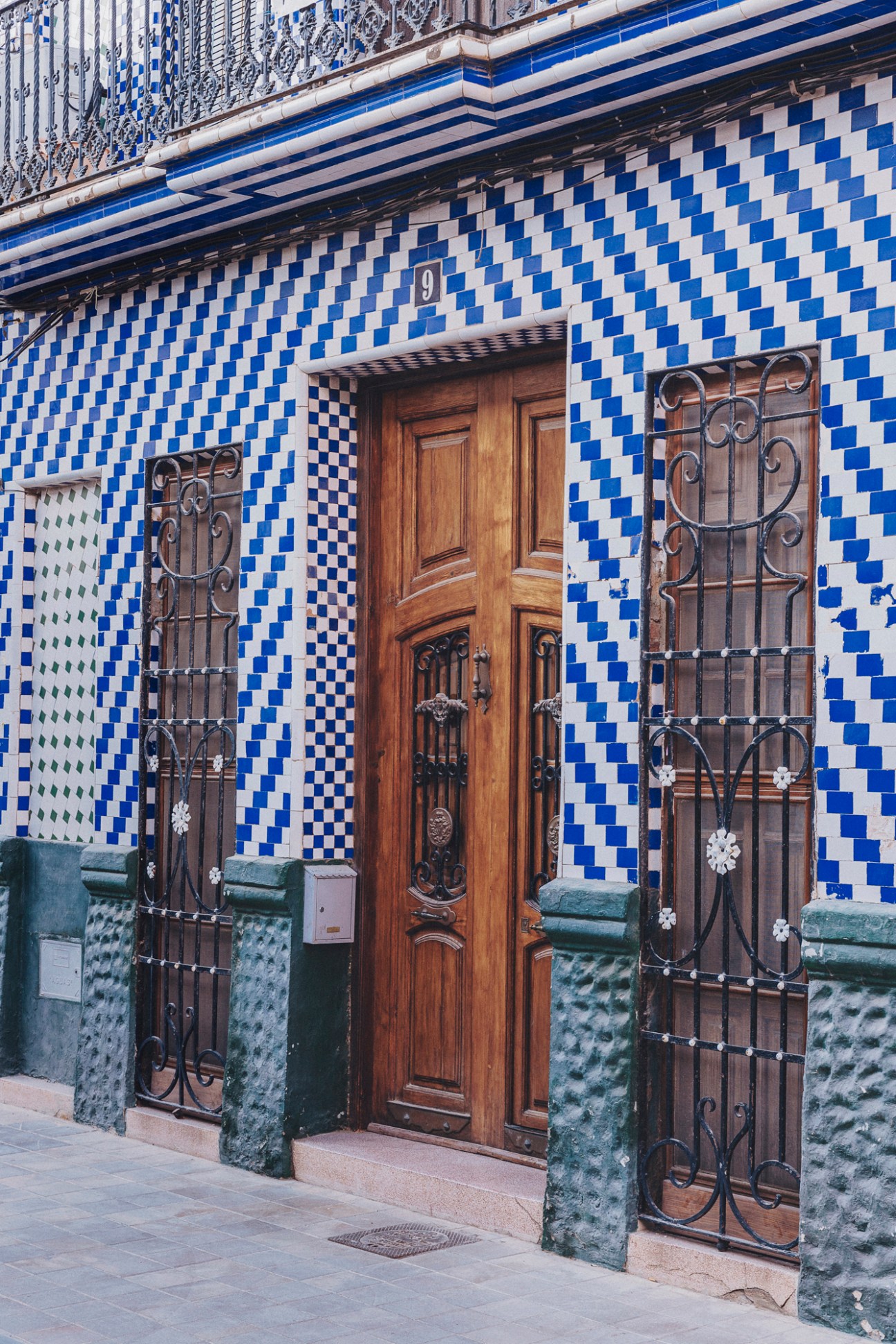 Blue and white checkered tile facade with ornate wooden door and decorative iron window grilles