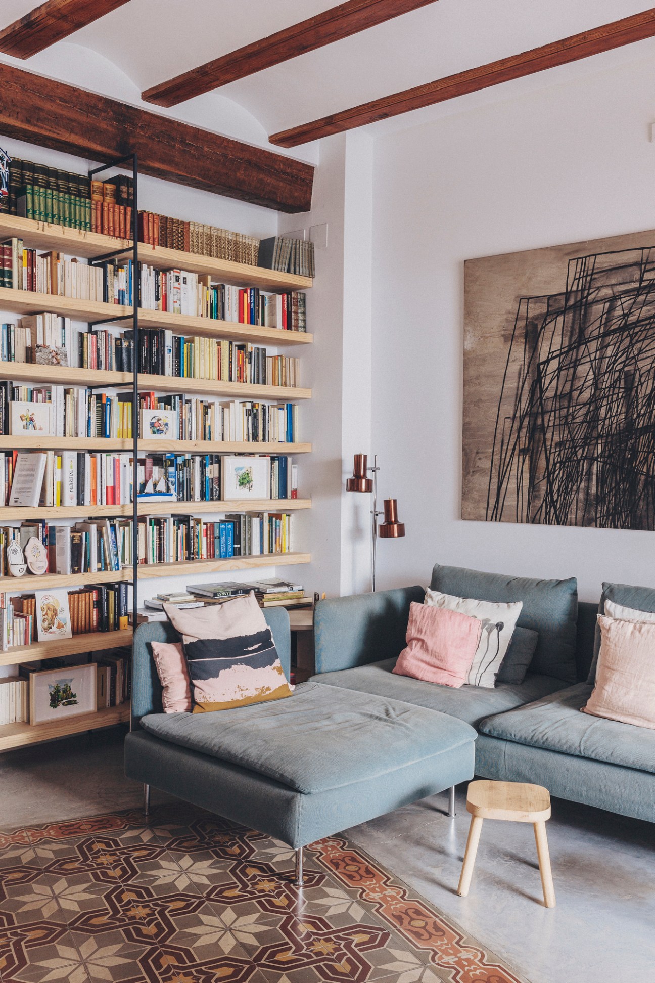 Modern living room with gray sectional sofa, built-in bookshelves, exposed wooden beams and geometric patterned floor