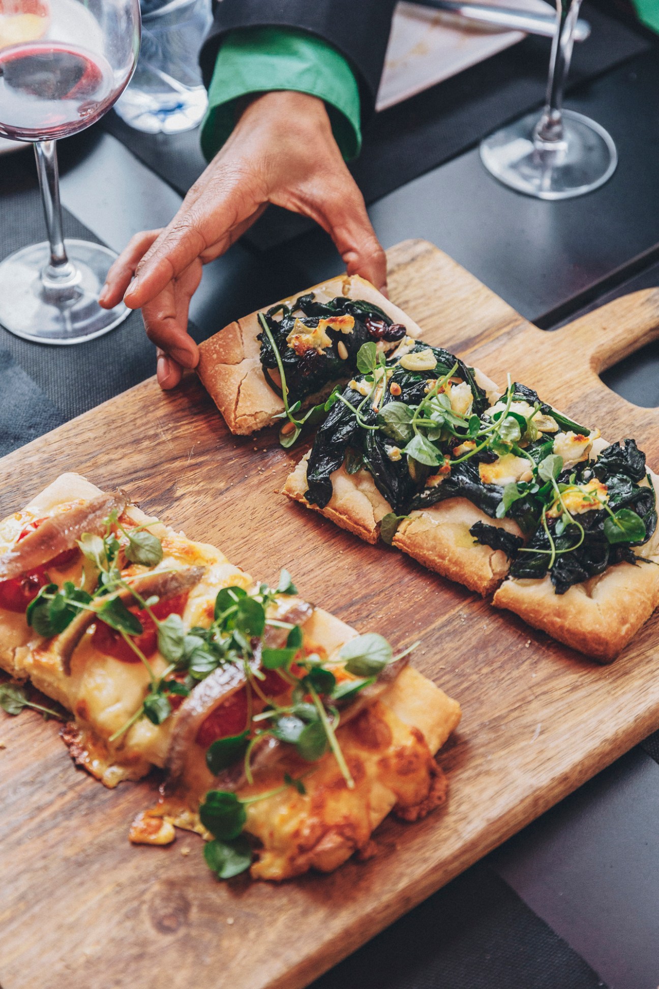 Hand hovering protectively over traditional Valencian cocas pastries topped with greens on wooden cutting board