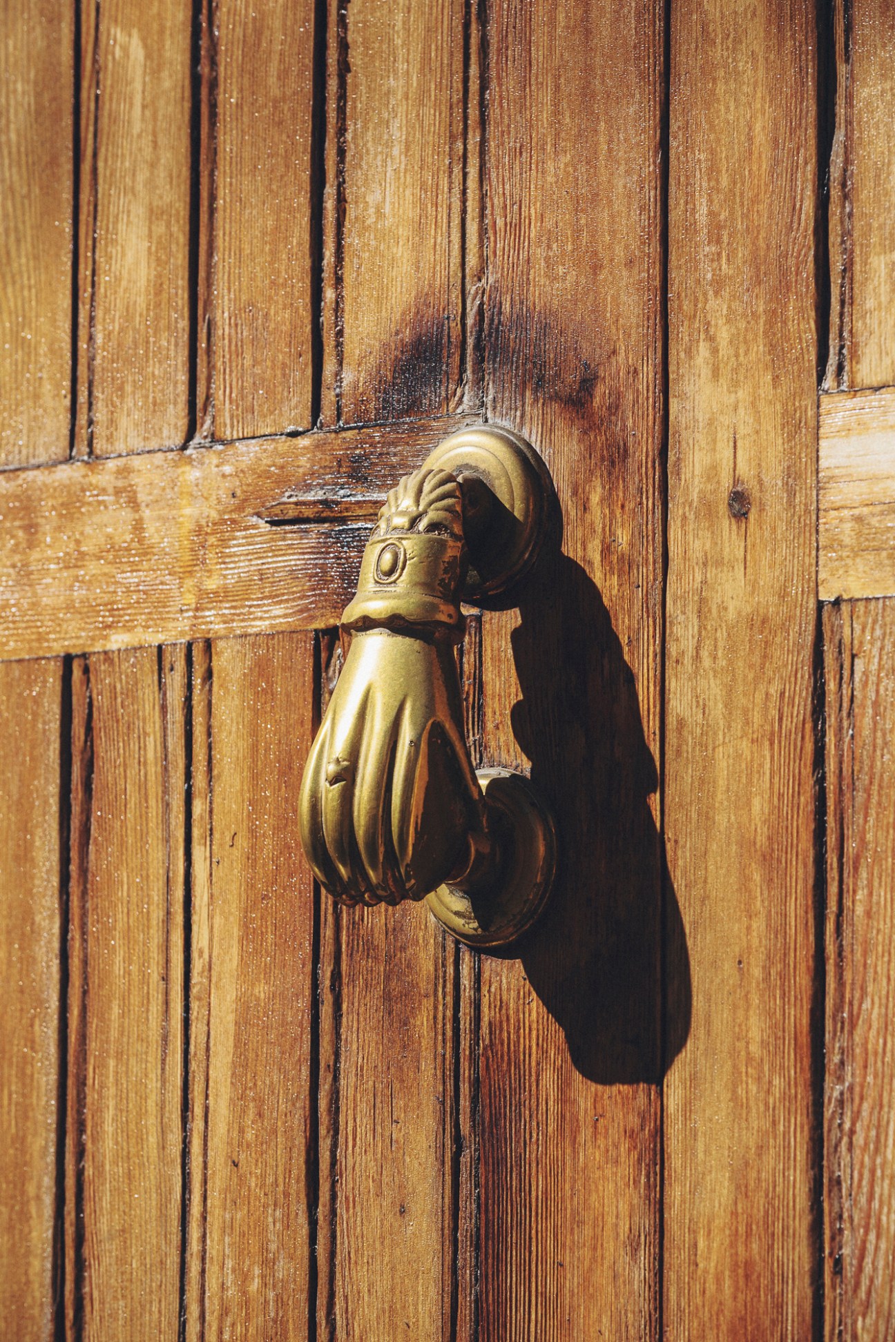 Ornate brass door knocker shaped like a hand on weathered wooden door