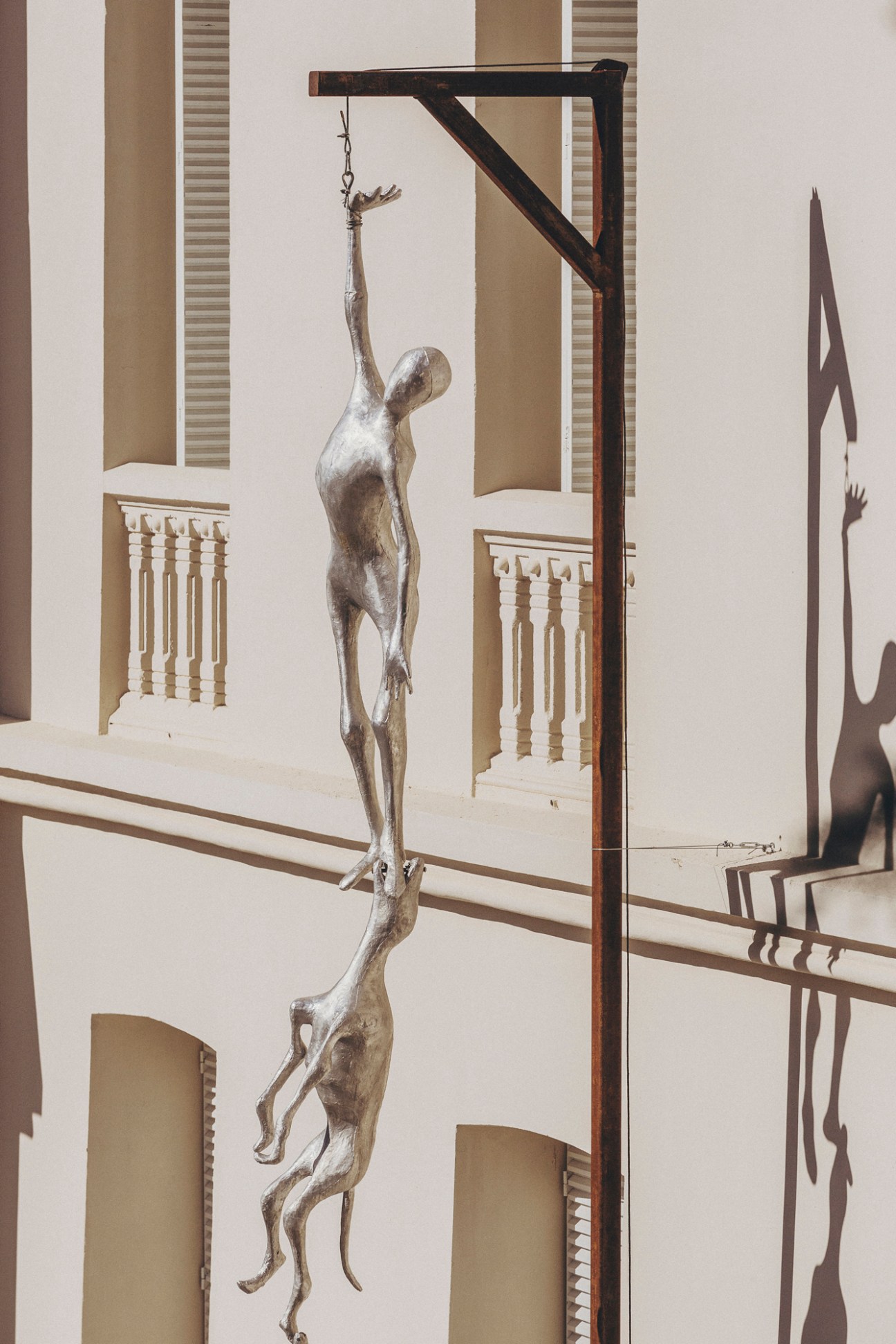 Bronze sculpture showing two human figures hanging from chains on a wooden gallows structure