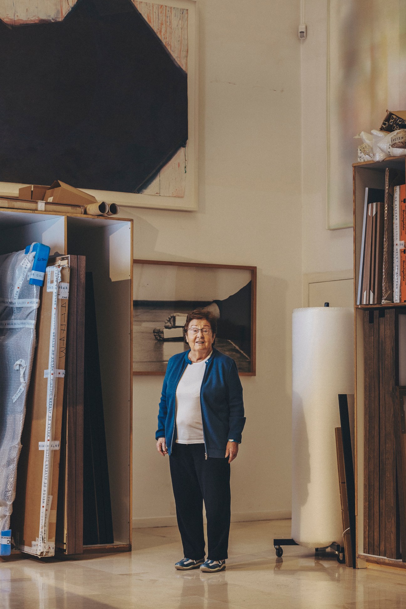 Helga de Alvear standing in her museum surrounded by storage racks and artwork