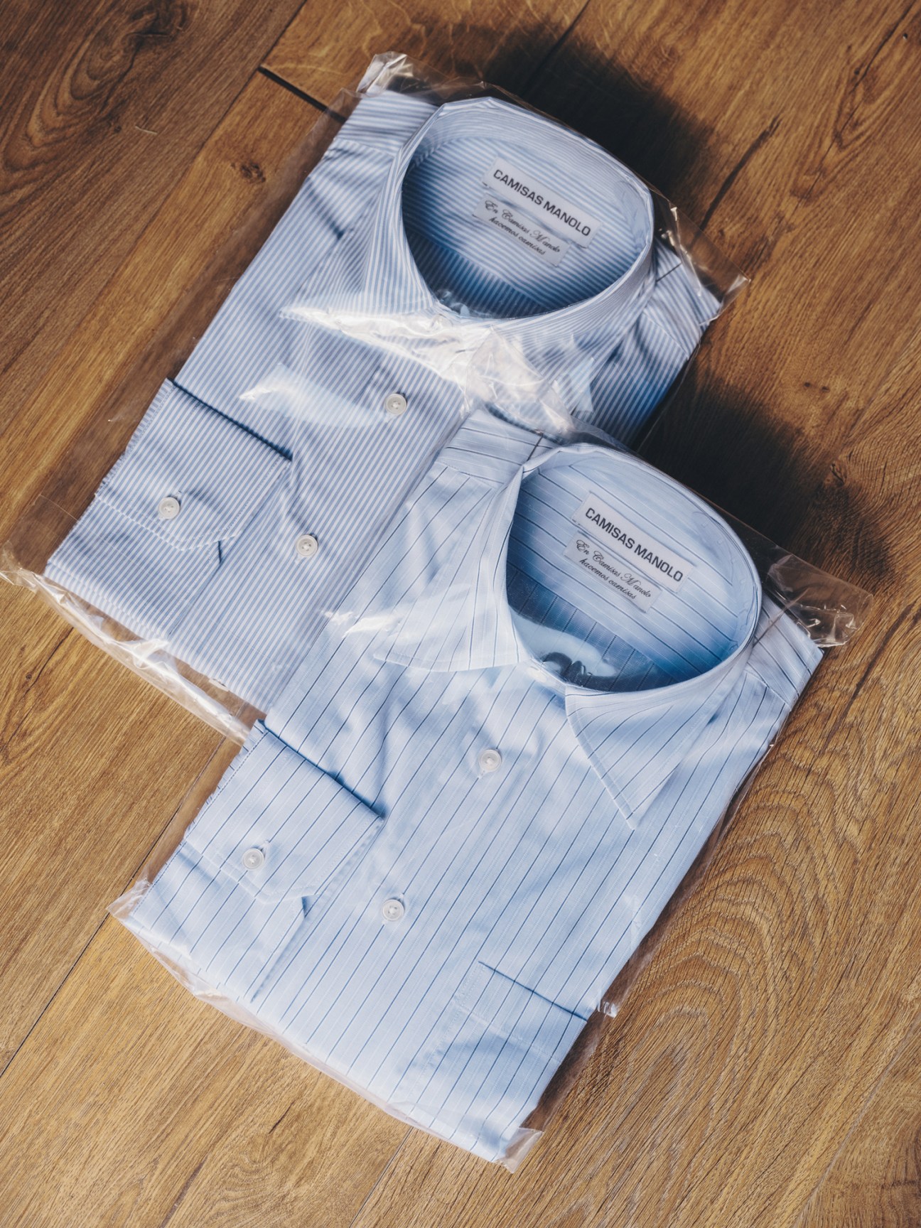 Two packaged Camisas Manolo dress shirts in clear plastic wrapping on wooden floor