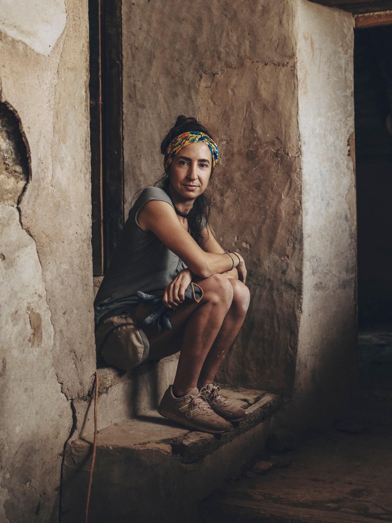 Miriam Estella sitting on stone steps wearing a colorful headband in a rustic building interior