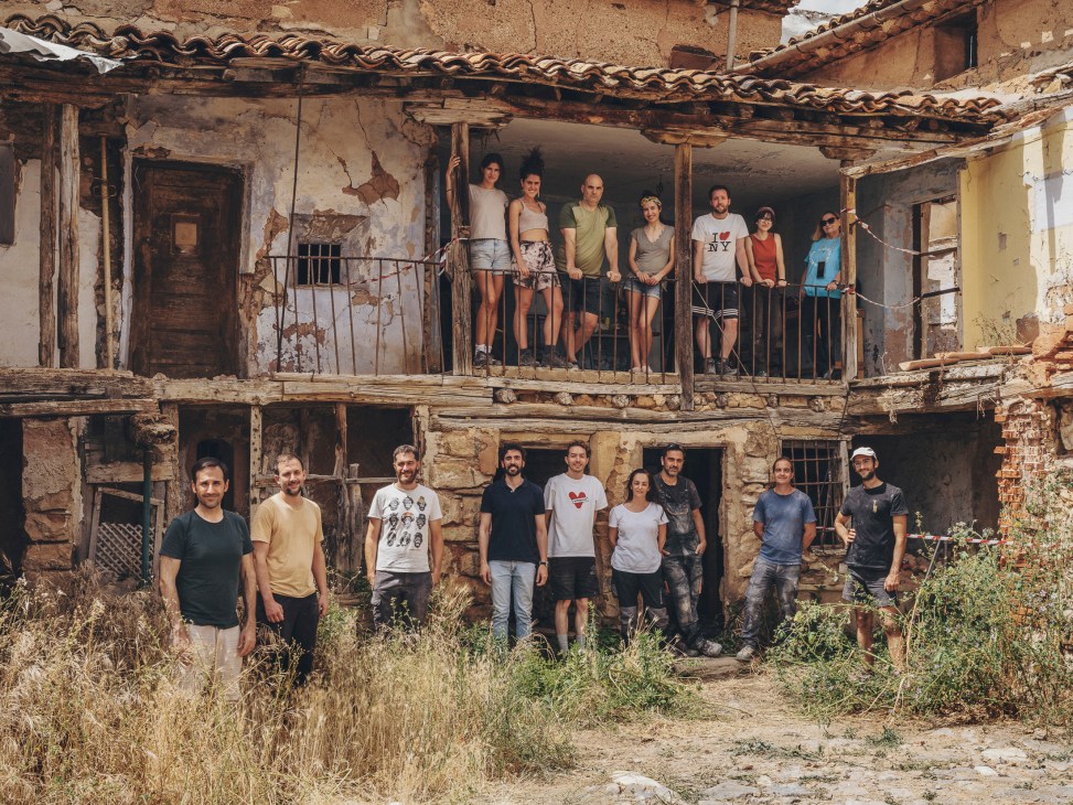 Group of workshop participants posing on balcony and ground level of rustic stone building with terracotta roof