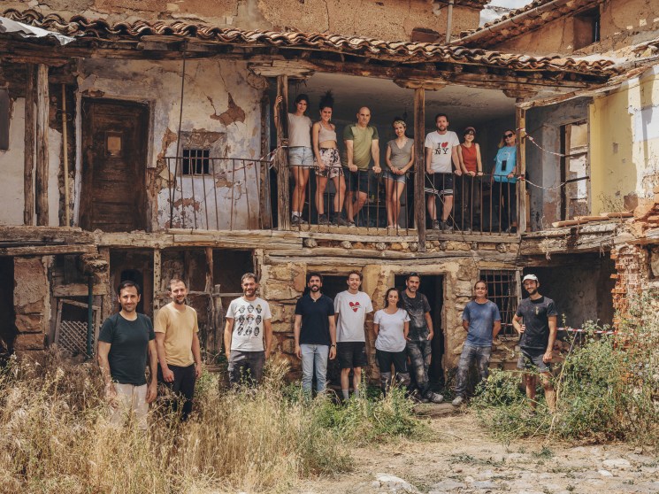 Group of workshop participants posing on balcony and ground level of rustic stone building with terracotta roof