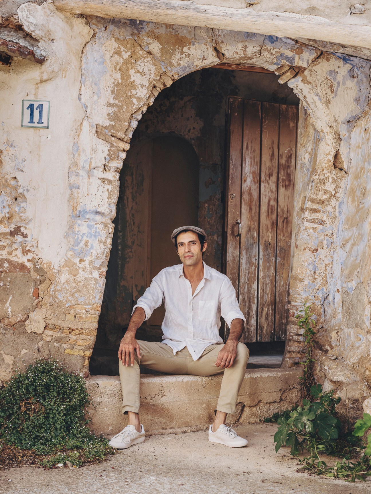 Alfonso Kint sitting on stone steps outside a traditional stone building with weathered wooden doors
