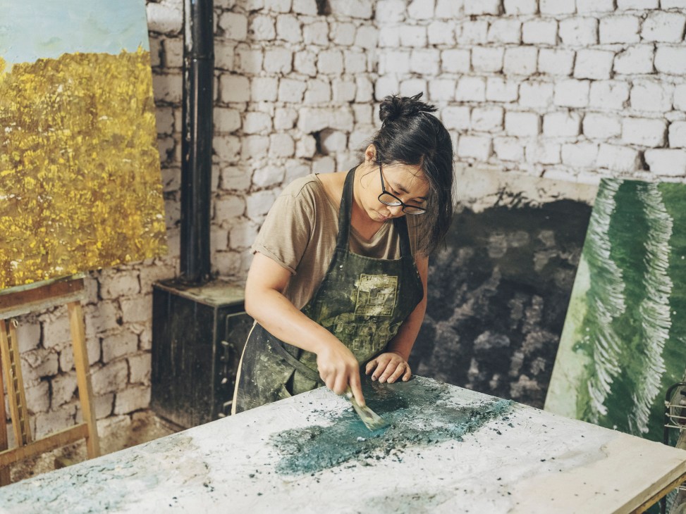 Artist Joo Eun Bae working on a large canvas in her home studio surrounded by paintings