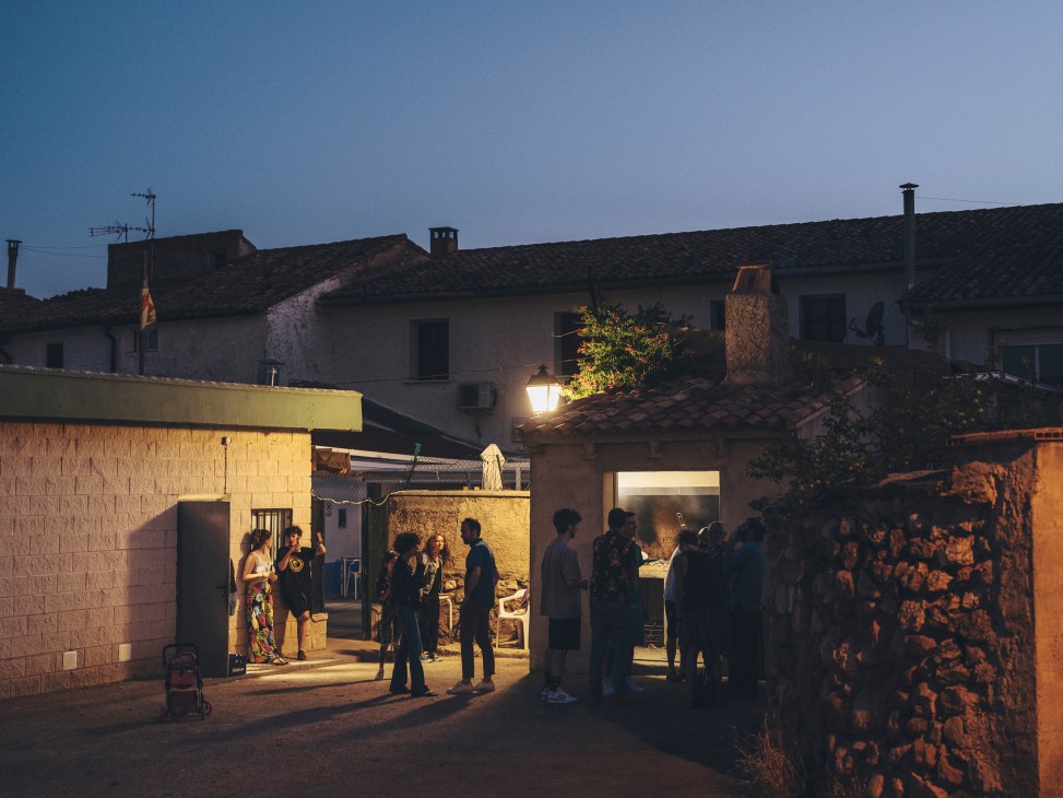 People socializing at outdoor tables with drinks at a village bar in rural Spain during evening hours