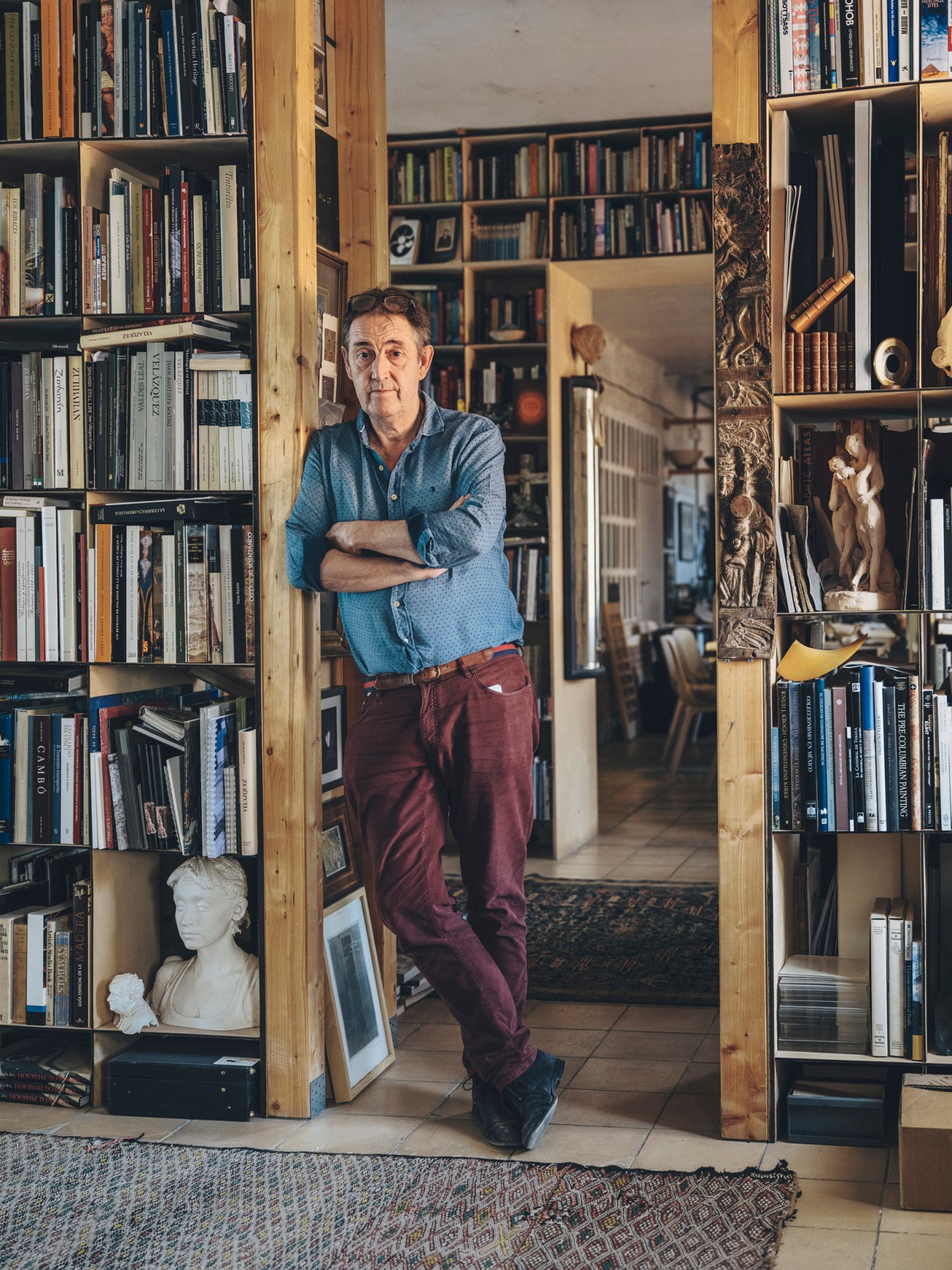 Adam Lowe standing in his library surrounded by floor-to-ceiling bookshelves filled with books and art objects