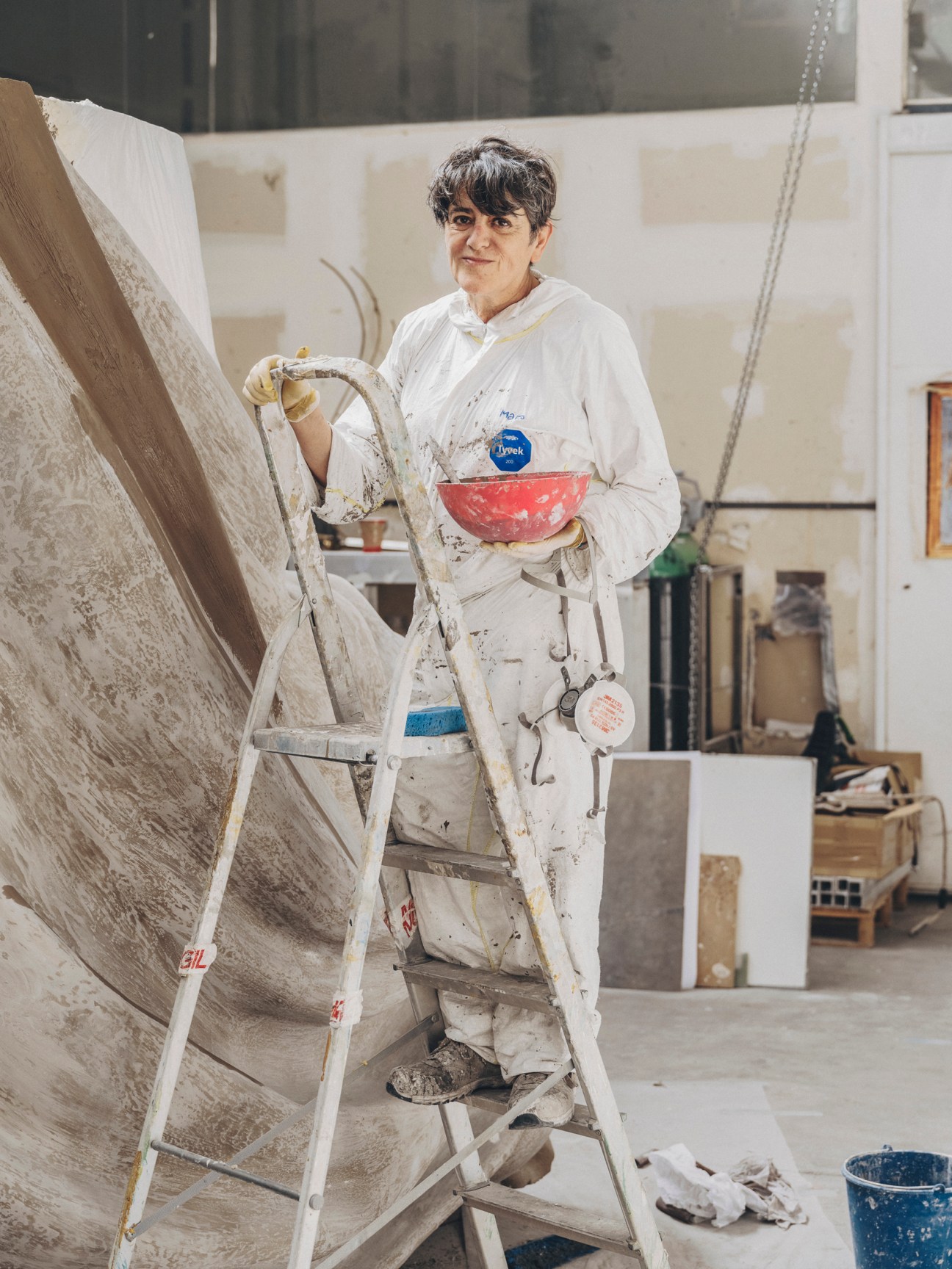 Mar García, moulder and painter at Factum Arte, standing on ladder holding paint bowl in white coveralls
