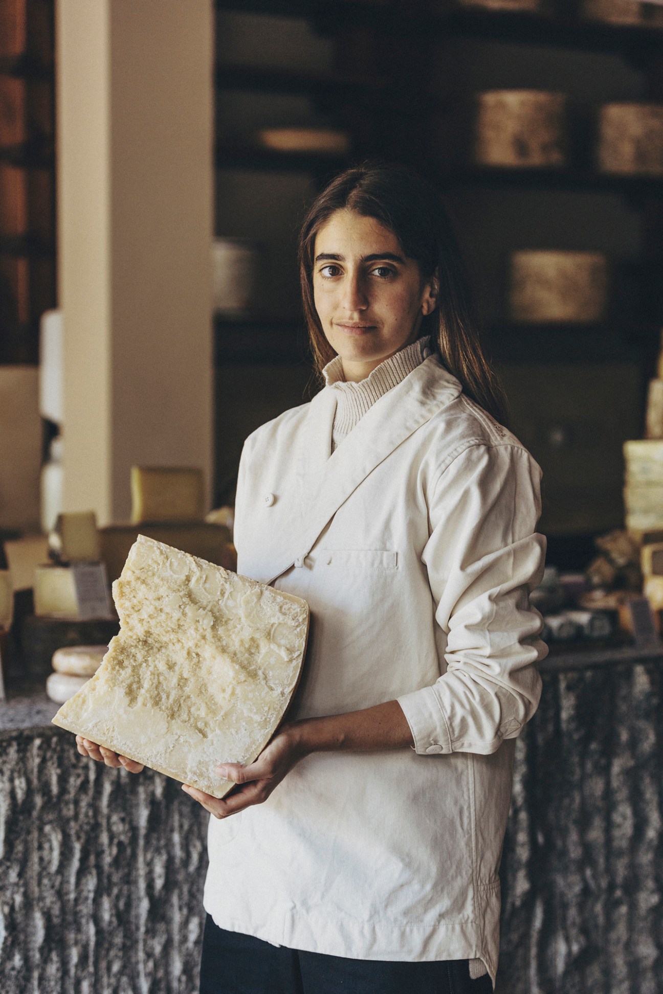 Woman in white chef's coat holding aged cheese wedge at Formaje Madrid