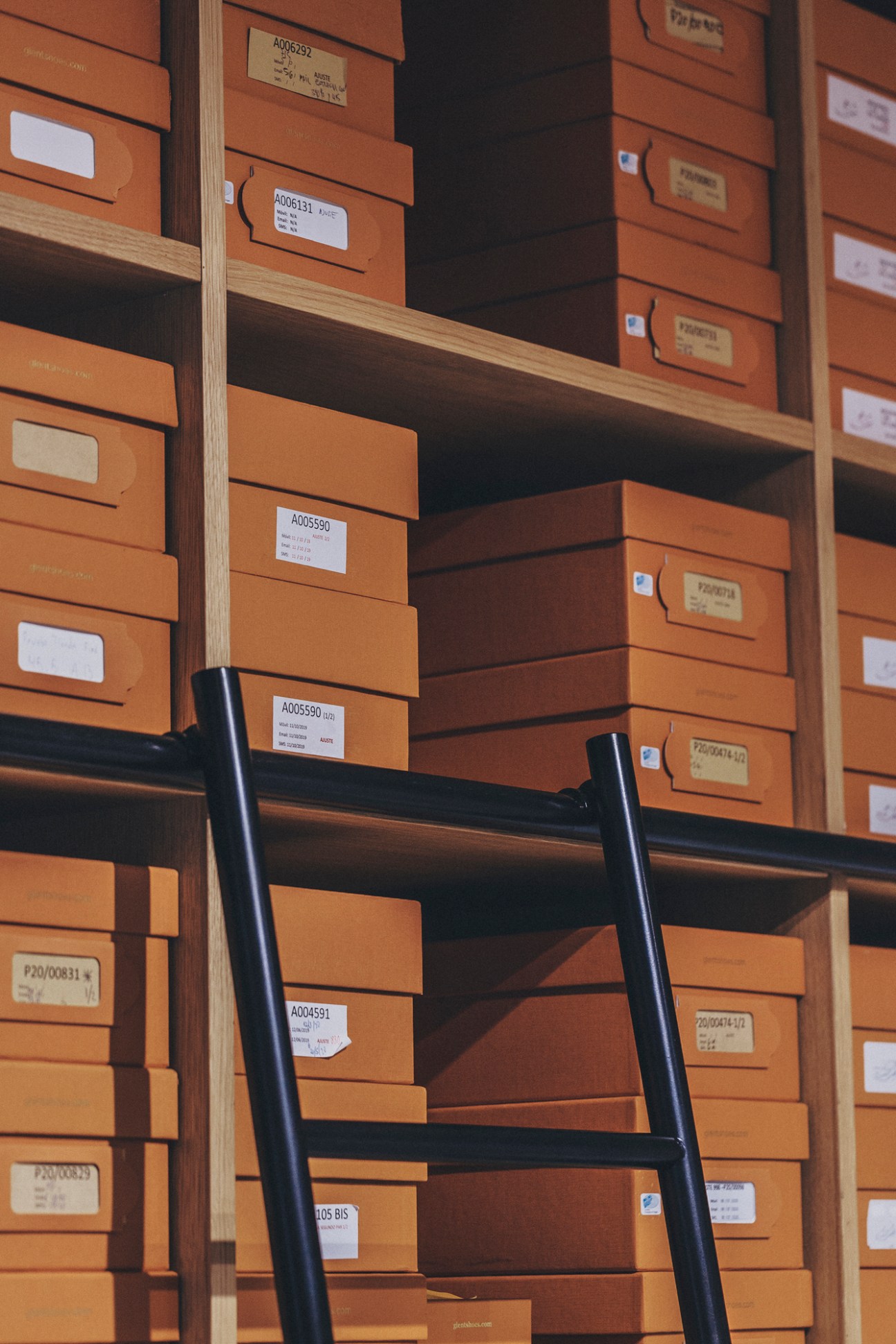 Wooden shelving unit filled with organized orange shoe boxes labeled with identification codes and a black ladder
