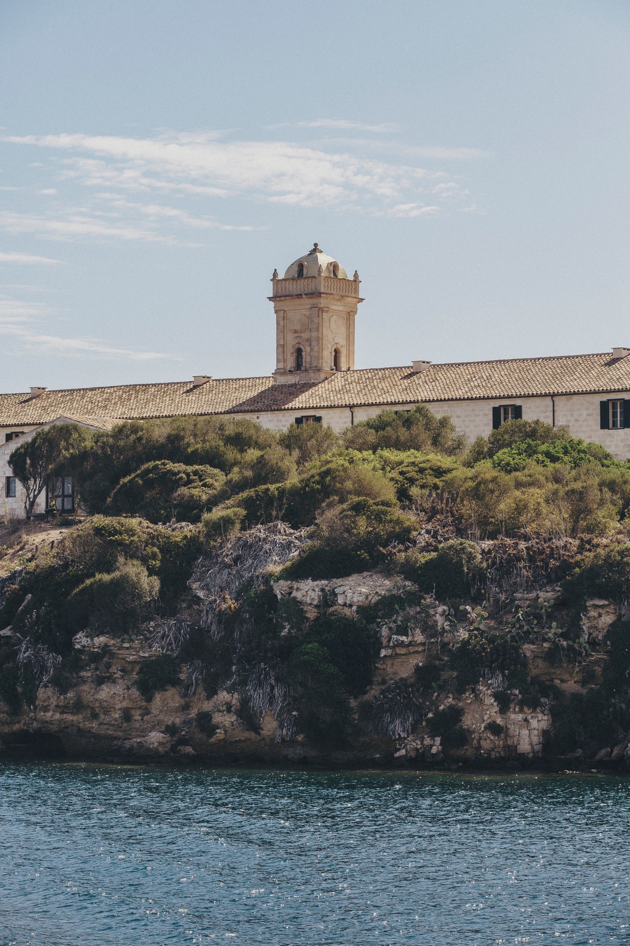 Historic stone building with bell tower overlooking water on Mediterranean coastline