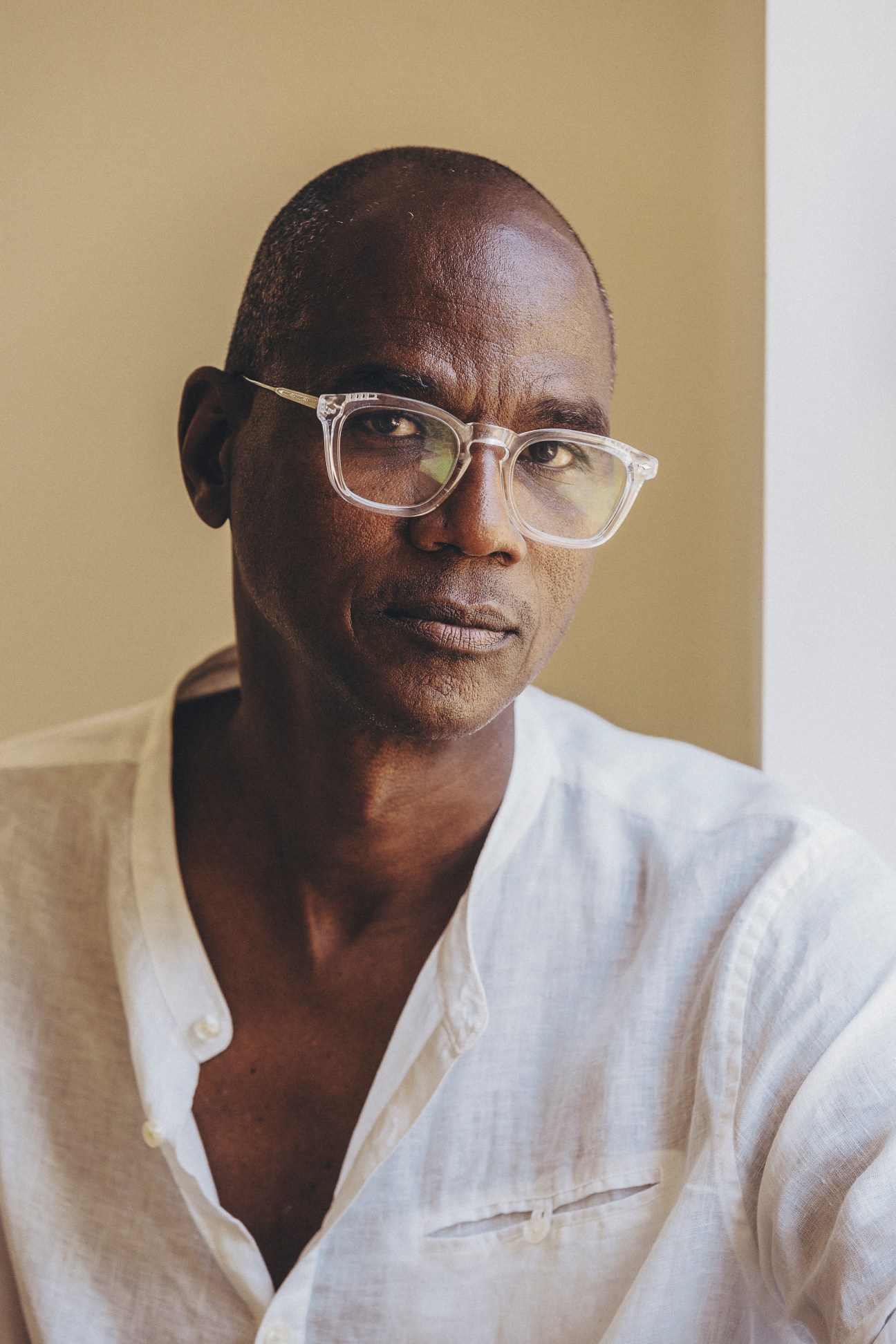 Black man with clear-framed glasses wearing white shirt against beige background