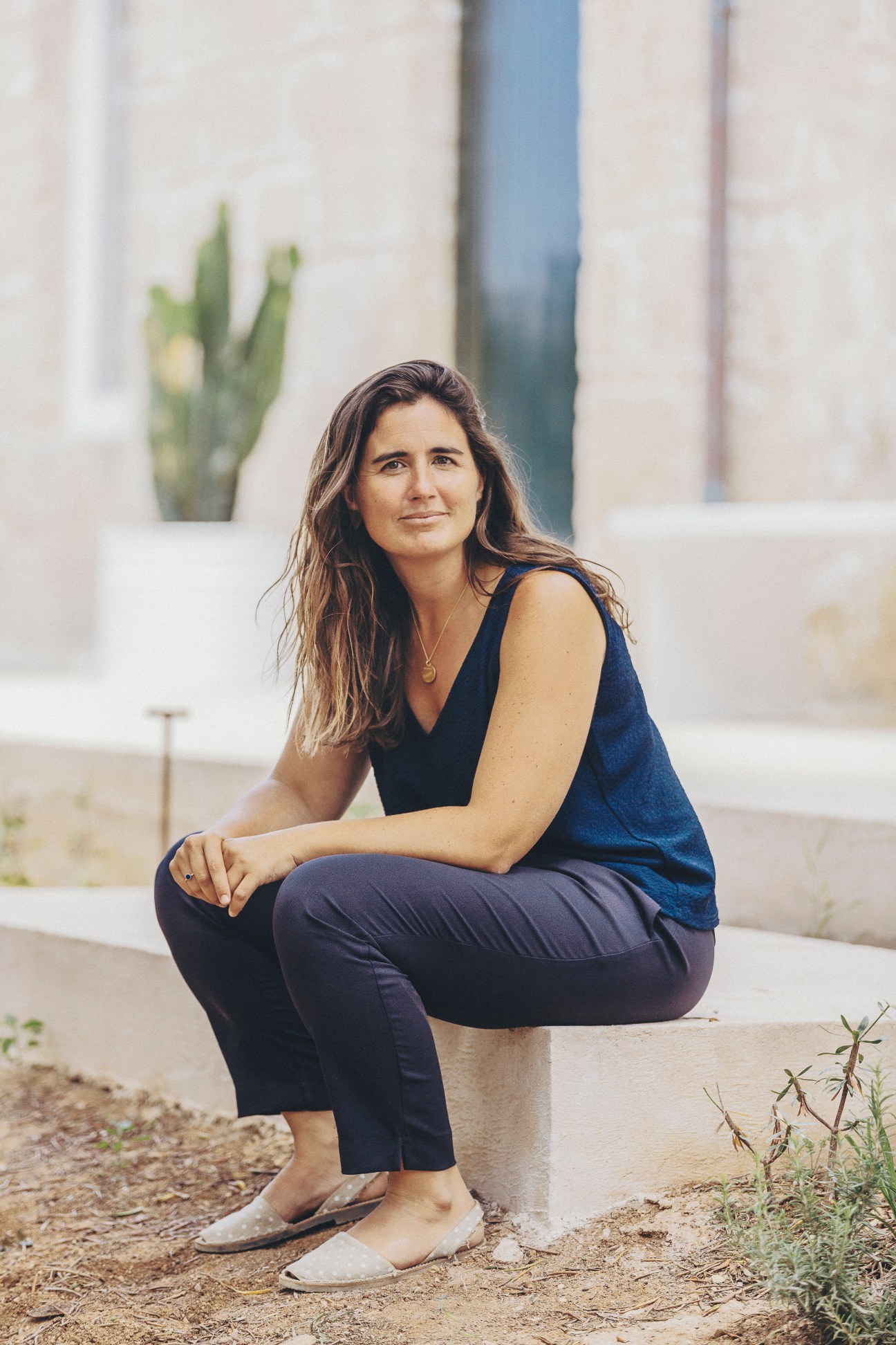 Woman in navy sleeveless top and dark pants sitting on concrete ledge outdoors