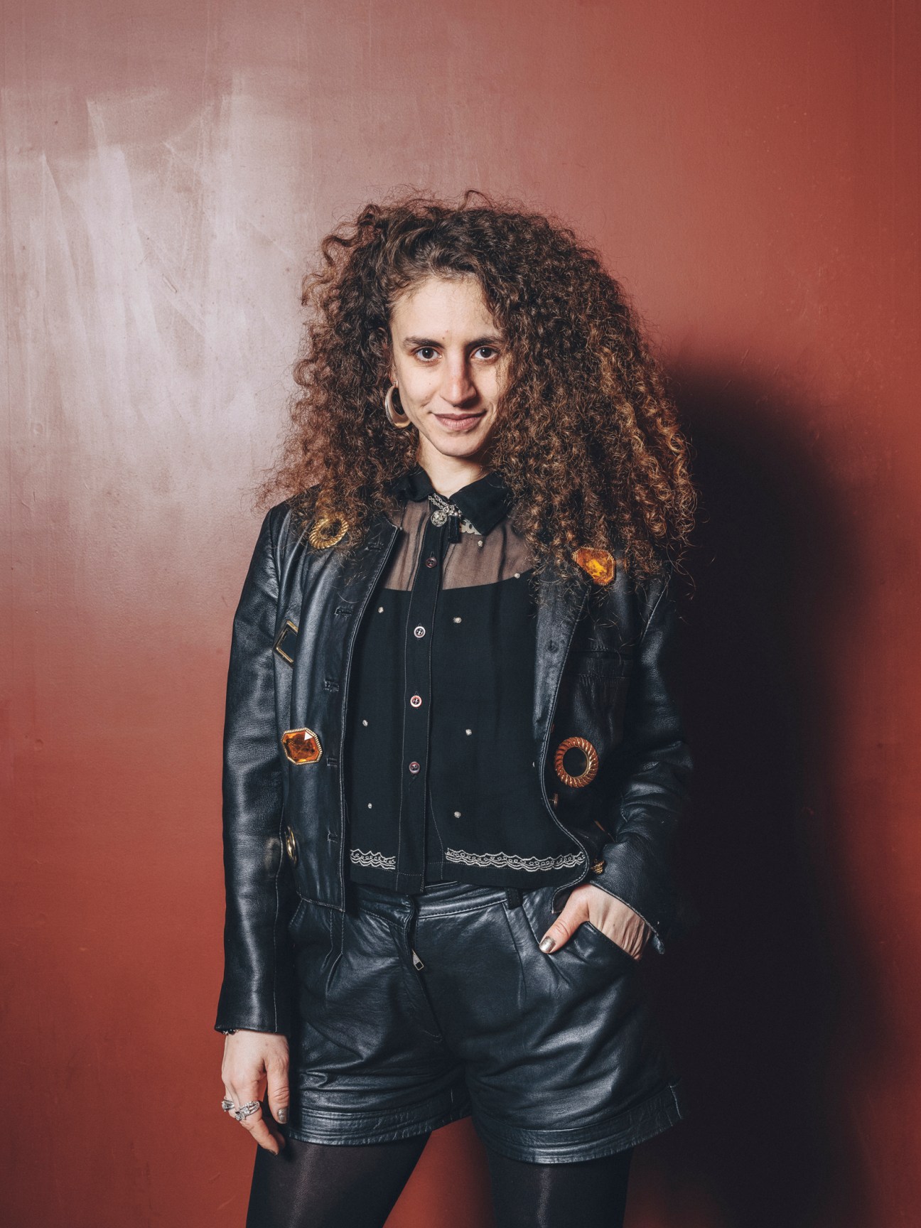 Sol wears a black leather jacket with decorative patches and matching leather shorts at La Paloma's carnival party