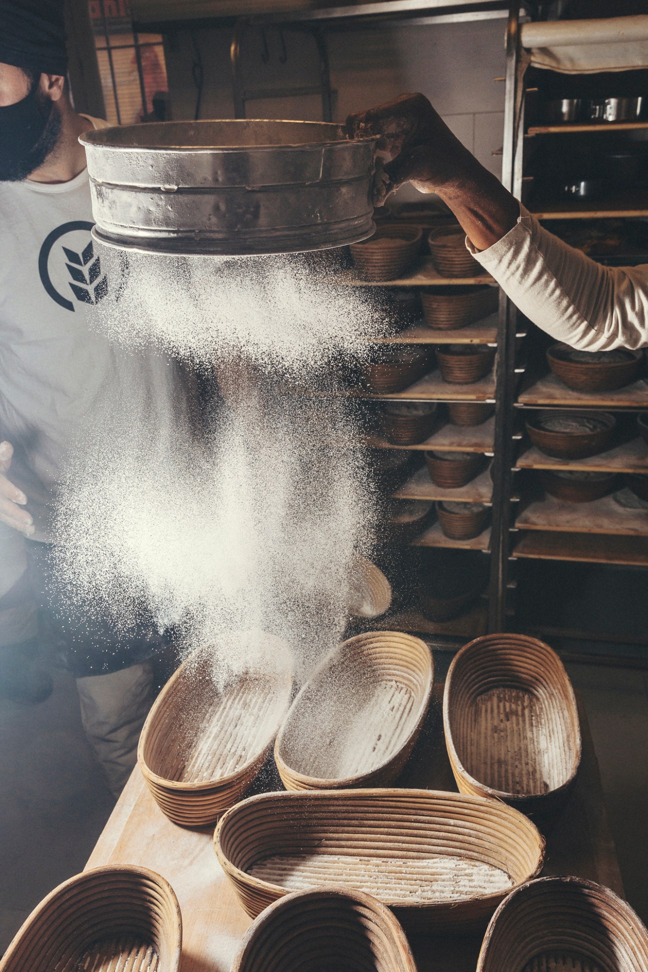 Baker's hands sprinkling flour into wicker proofing baskets at Obrador San Francisco