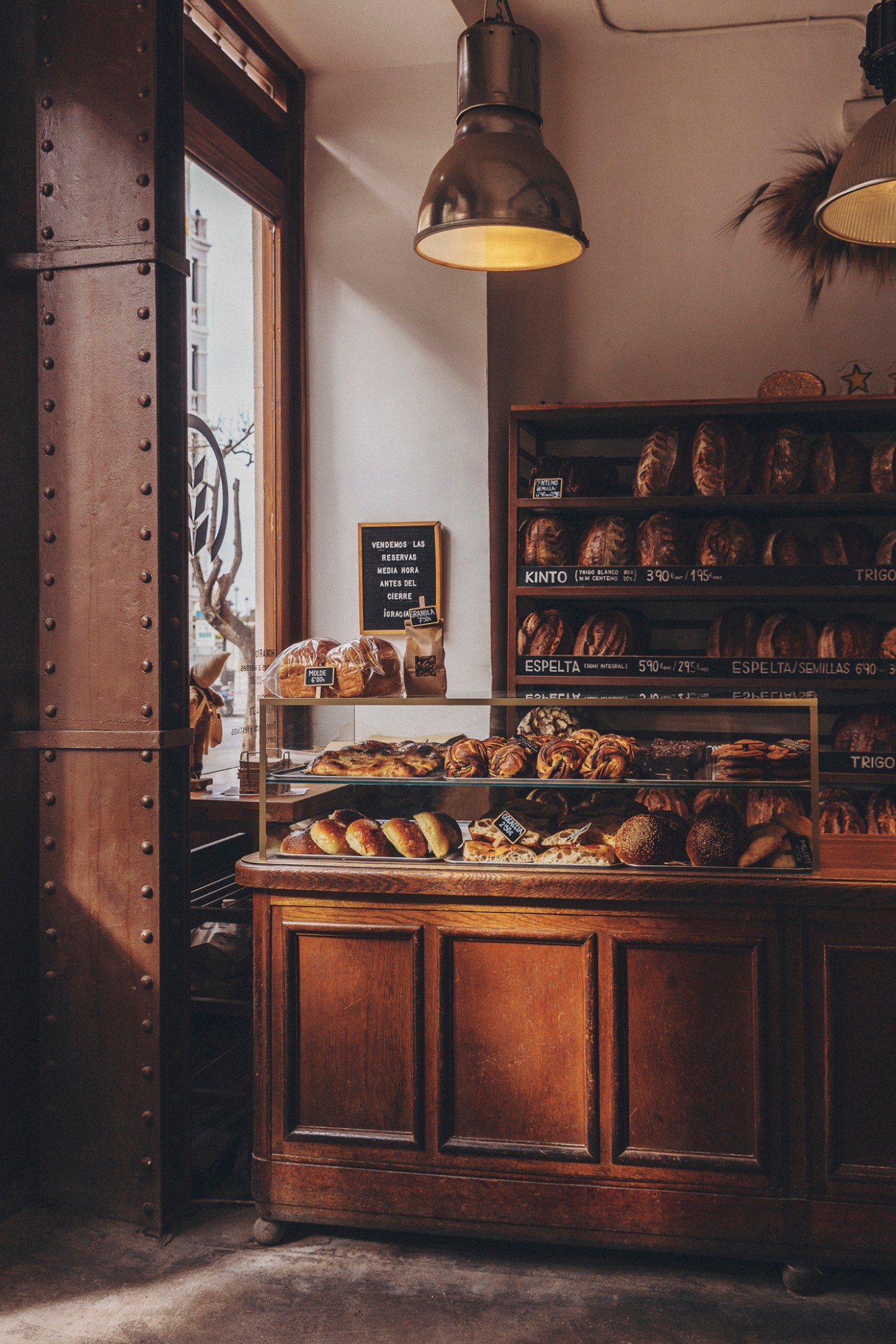 Interior of Obrador San Francisco bakery showing wooden display case with various breads and industrial pendant lighting