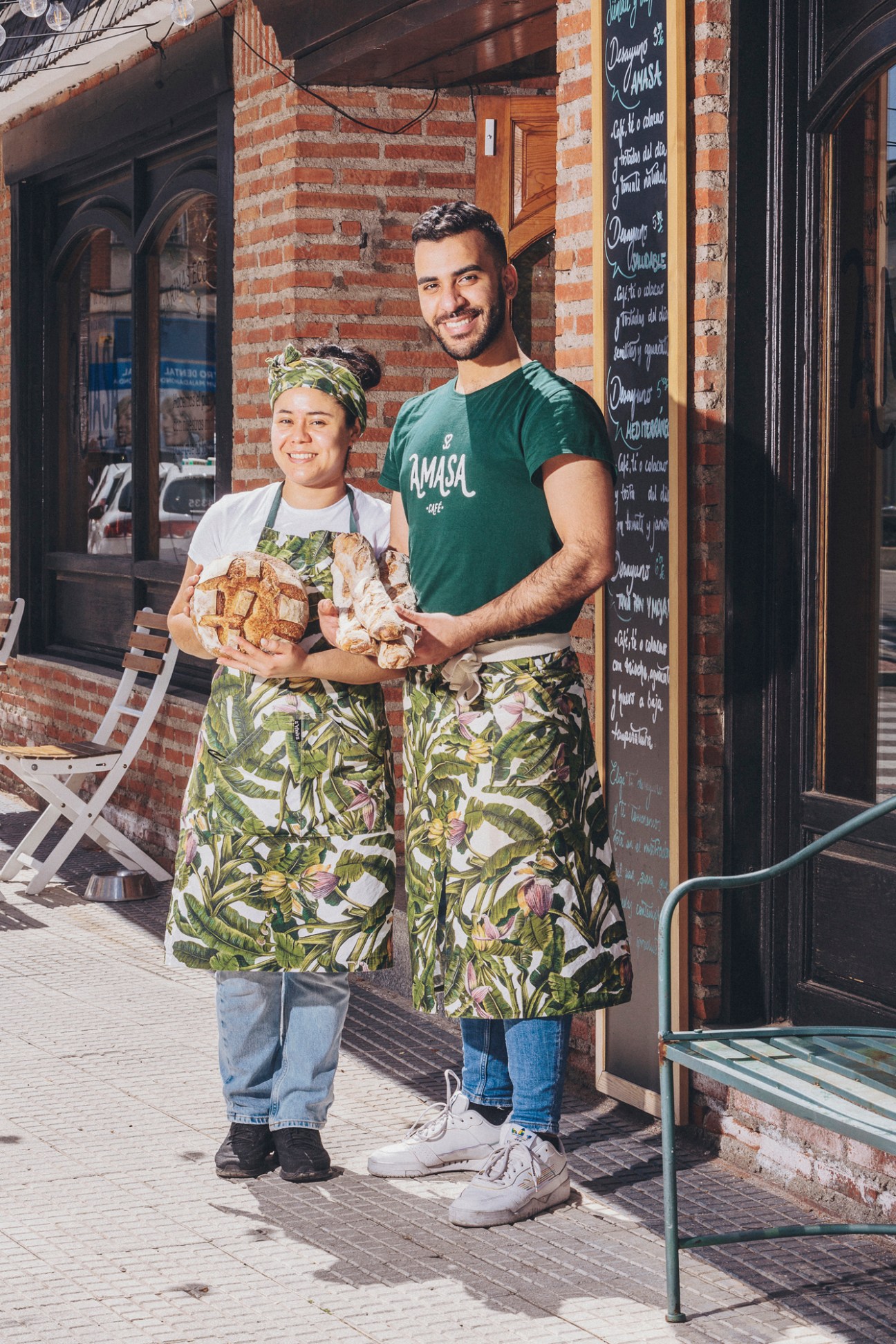 Reina and David of Amasa bakery standing outside their shop wearing matching tropical print aprons