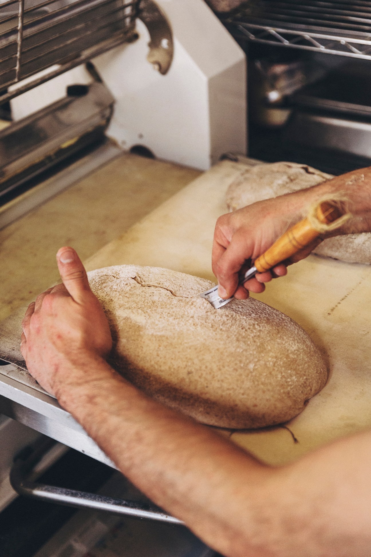 Baker's hands using a scoring tool to make cuts in bread dough at Alma Nomad bakery