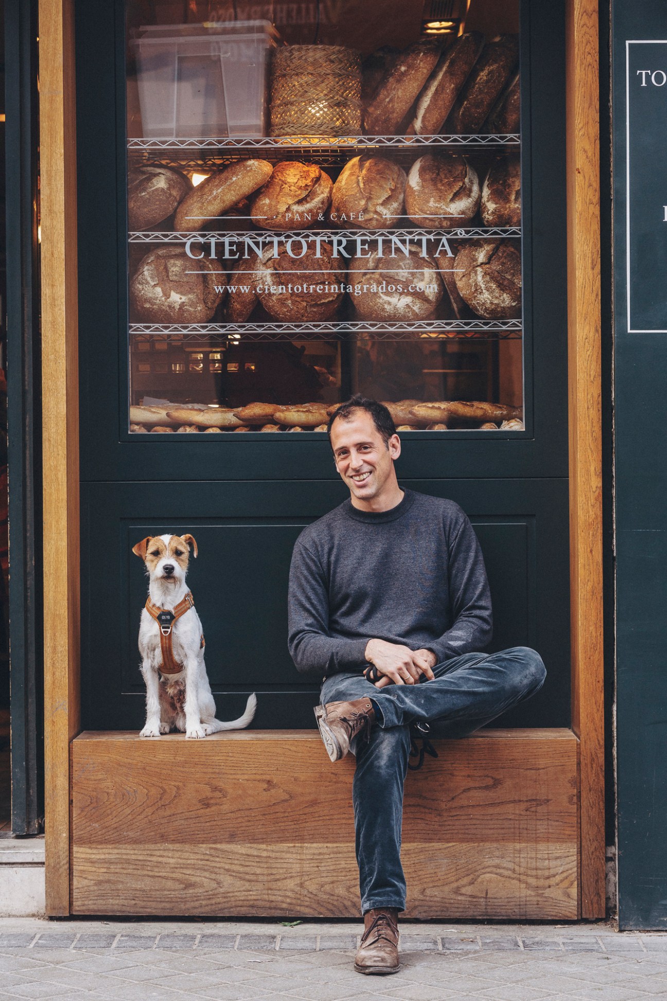 Guido Miragoli sitting in bakery doorway with small terrier dog beside him at Cientotreinta Grados
