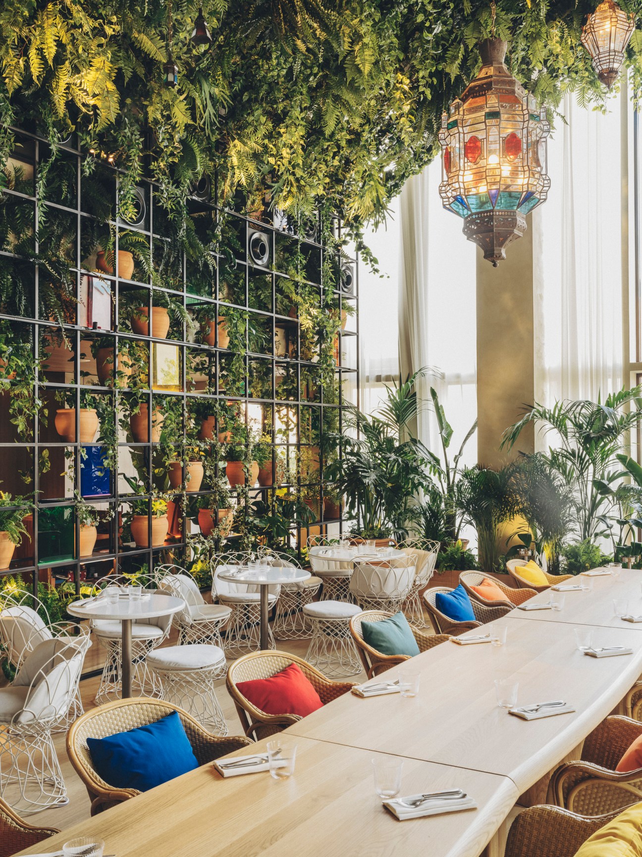Restaurant dining area with lush greenery, colorful wicker chairs, white tables and ornate hanging lantern