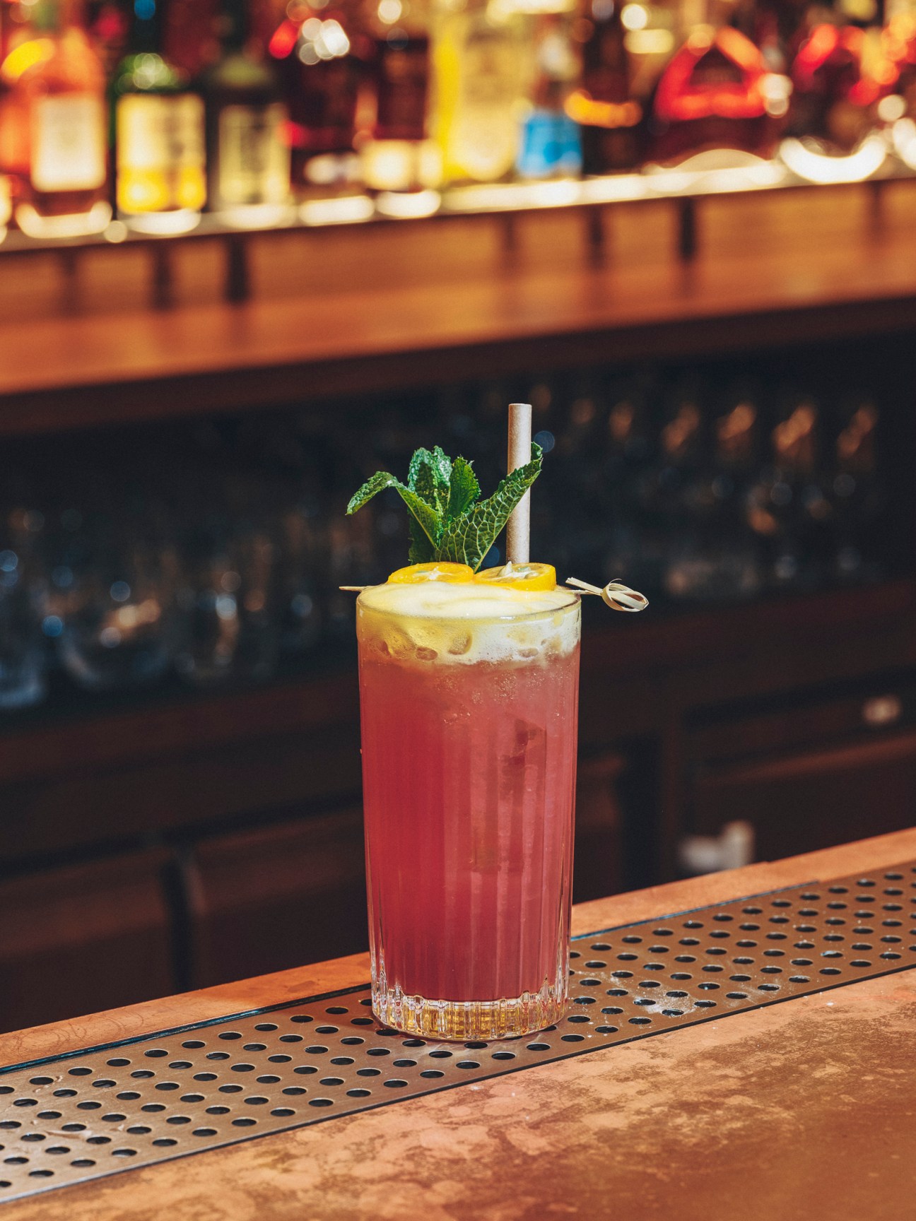 A layered cocktail with red and yellow colors, garnished with mint and served with a straw at a bar