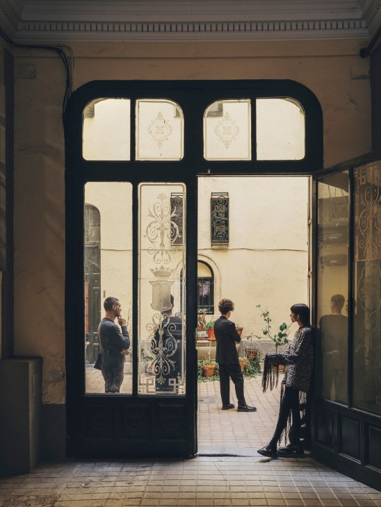 N-E studio entrance with staff members visible through ornate black-framed glass doors in a 19th-century Madrid palace.
