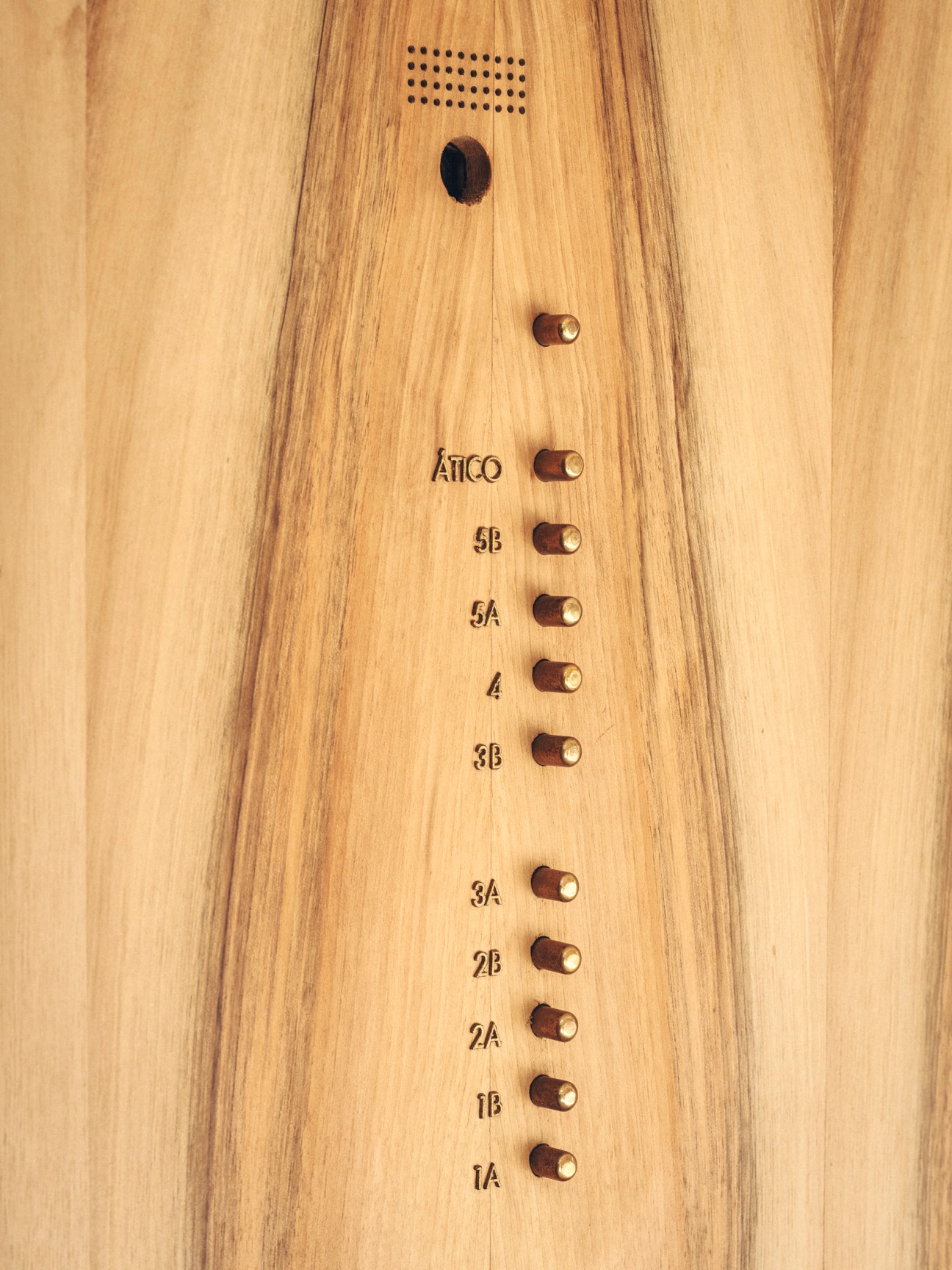 Wooden intercom panel with brass buttons labeled 1A through 5B and ATICO