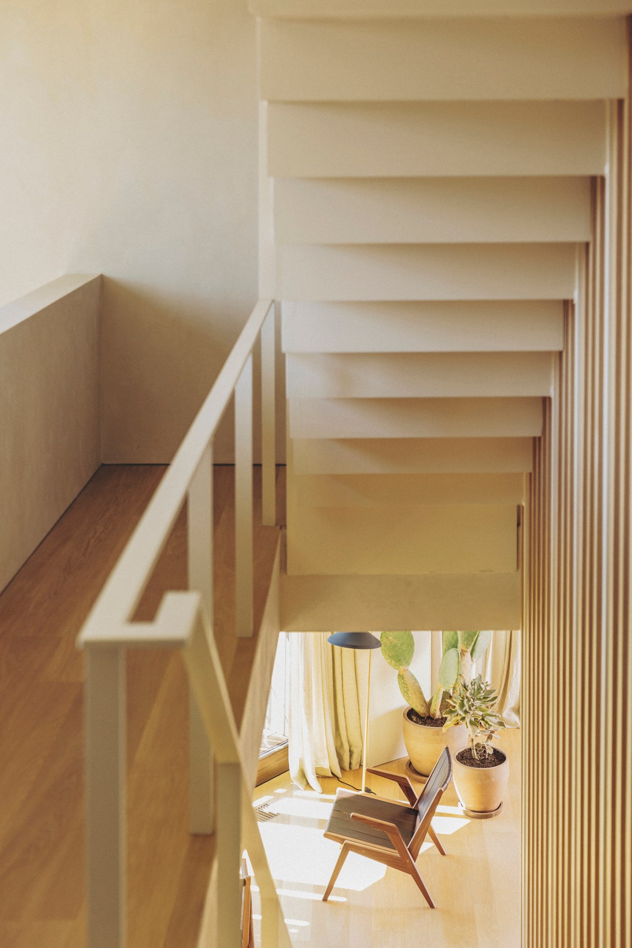 Landing and stairwell with light wood stairs and handrail, white walls, and plants visible below