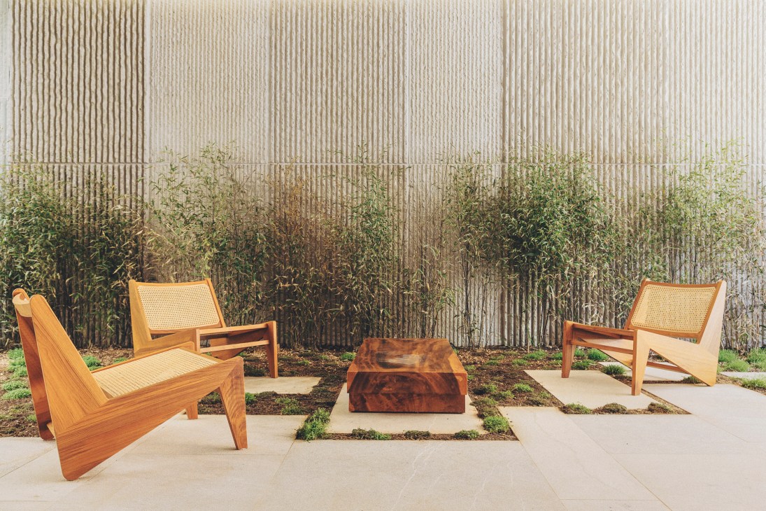 Modern outdoor terrace with wooden chairs featuring cane backs and a dark wood coffee table on concrete pavers