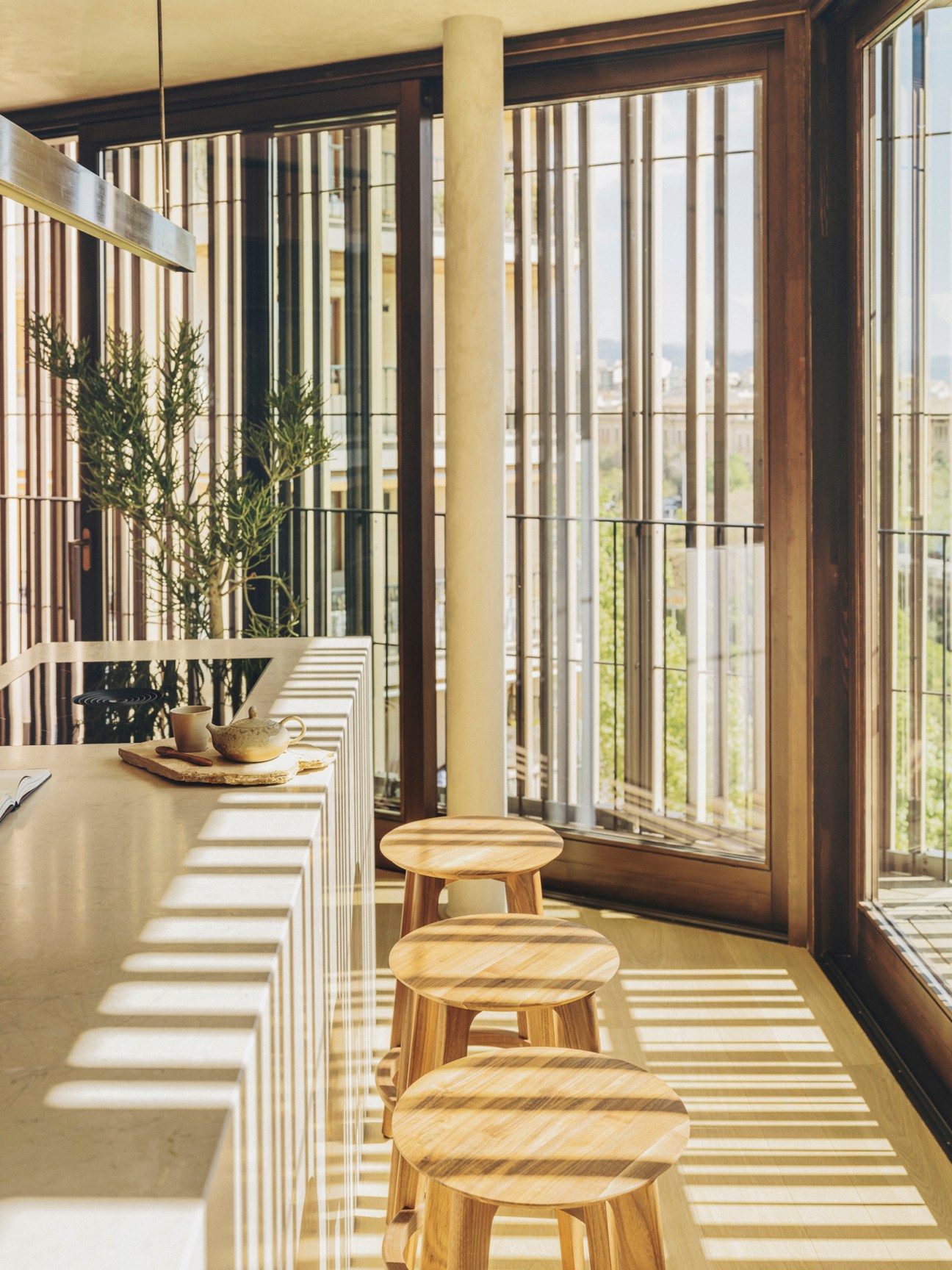 Kitchen counter with wooden bar stools and timber slat window screening casting striped shadows