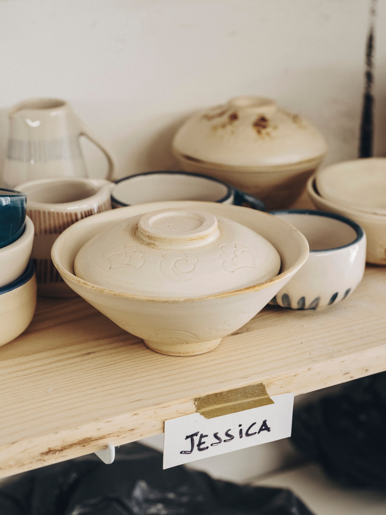 Various ceramic bowls and pottery pieces on wooden shelf with Jessica name tag
