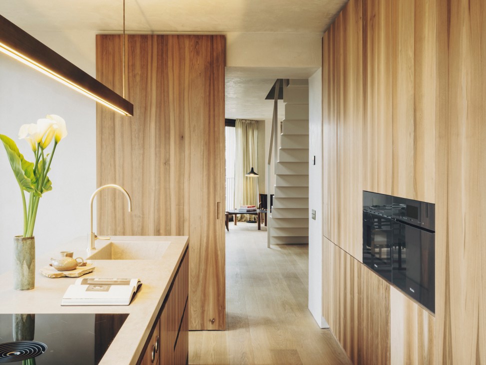 Modern kitchen with light wood cabinets, white countertops, brass fixtures and lime-mortar walls
