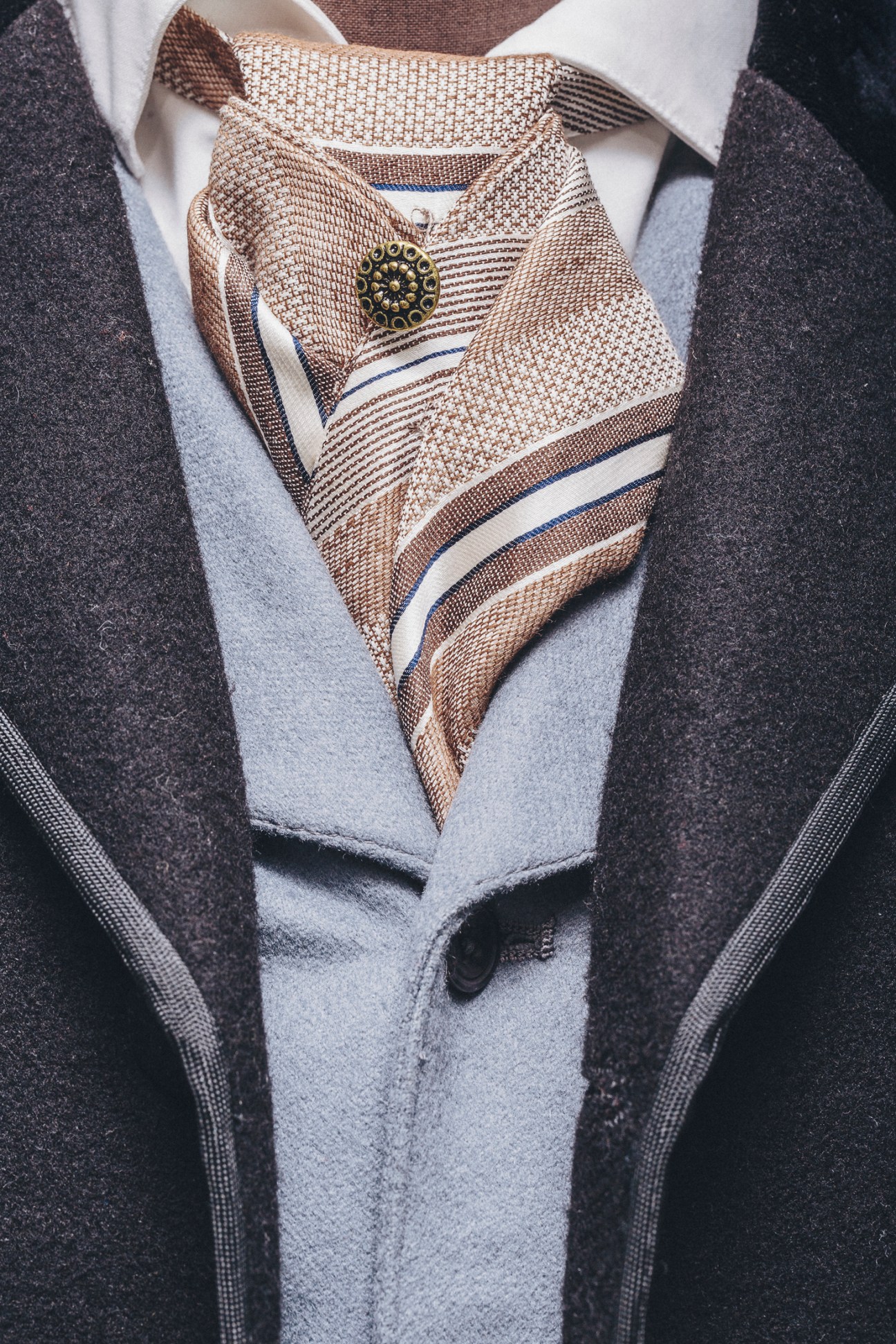 Close-up detail of an ornate brown and cream striped morning coat with decorative pin being crafted for The Gilded Age