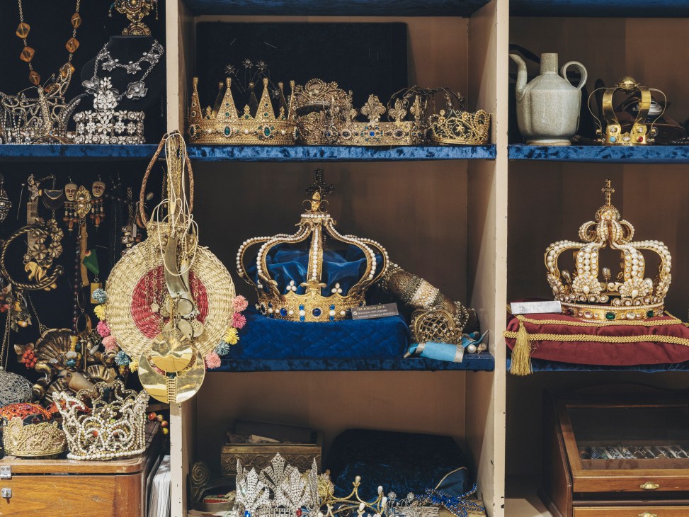 Collection of ornate crowns, tiaras and decorative jewelry displayed on shelves in storage cases