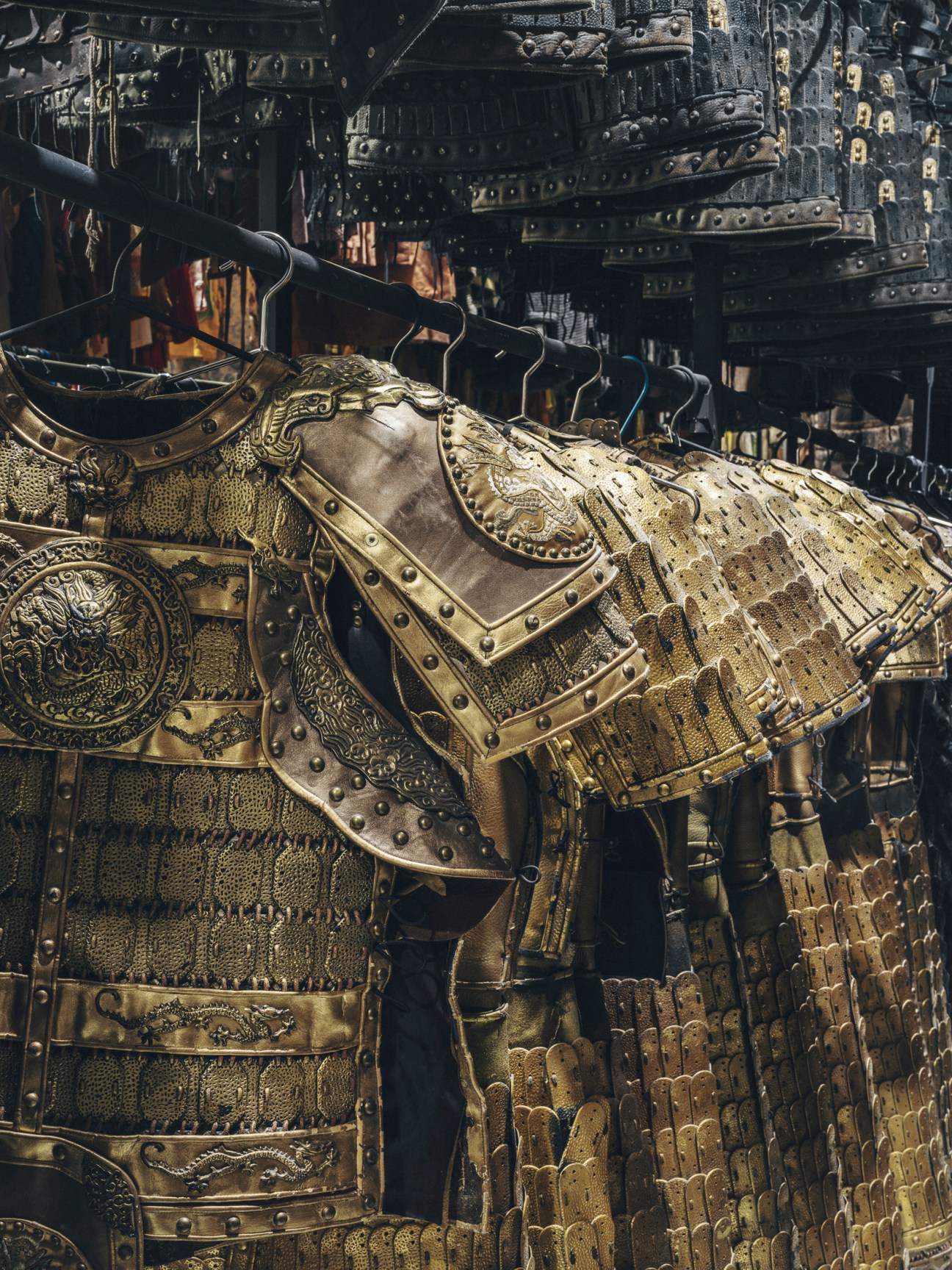 Ornate golden armor with detailed engravings and metalwork displayed on mannequins in costume warehouse