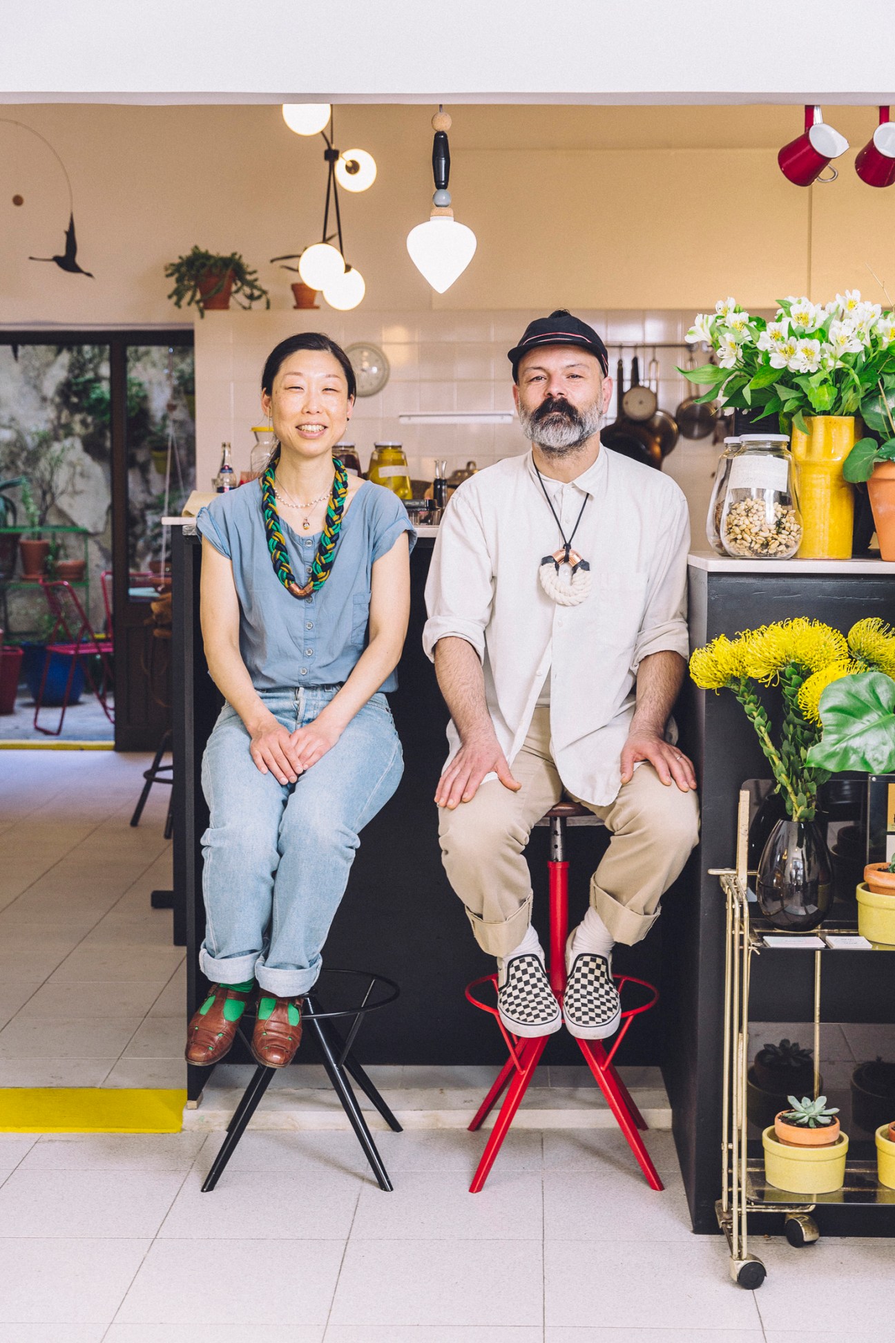 Sako Arao and Miguel Cunha seated in their restaurant Namban Oporto Kitchen with plants and hanging lights.