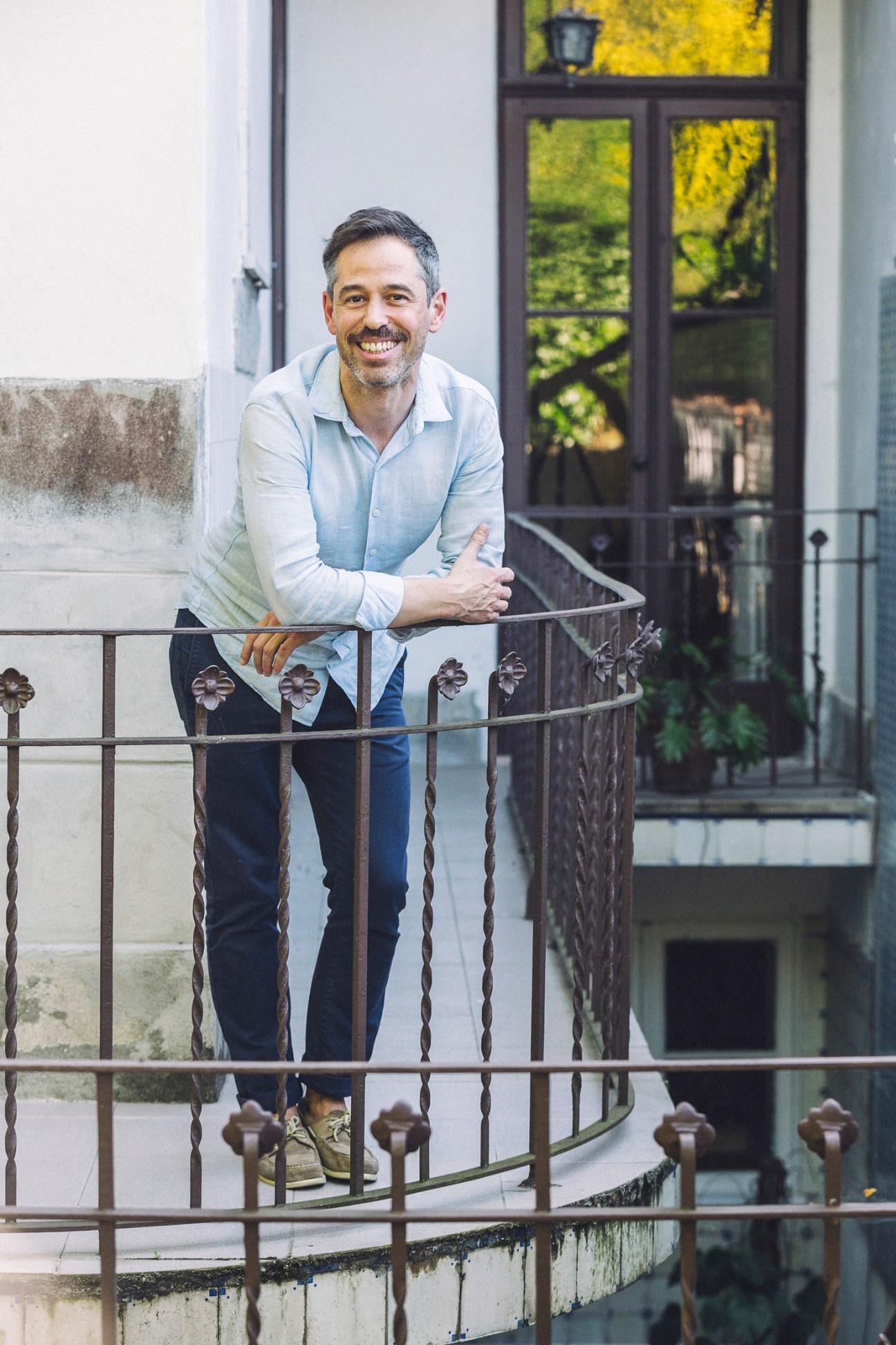 Man smiling while leaning against an ornate wrought-iron railing on a residential balcony in Porto.