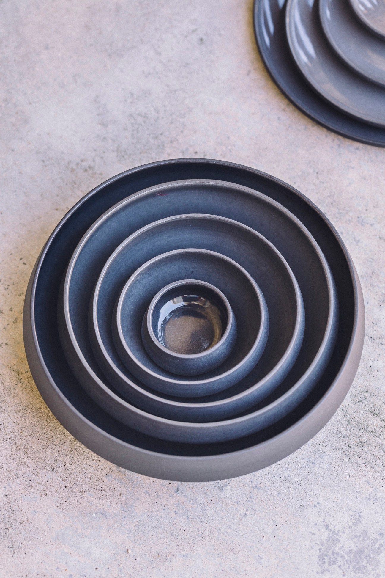 Nested ceramic bowls in shades of blue and grey arranged concentrically on a concrete surface.