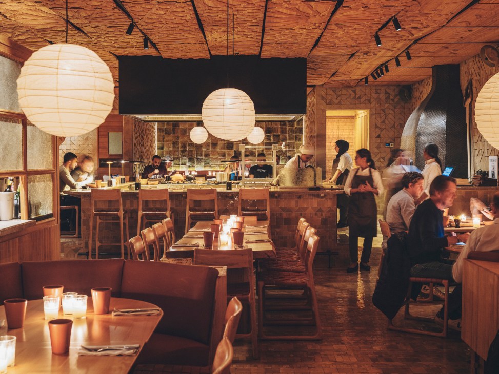 Restaurant dining room during evening service with warm ambient lighting, paper lanterns, and diners at wooden tables